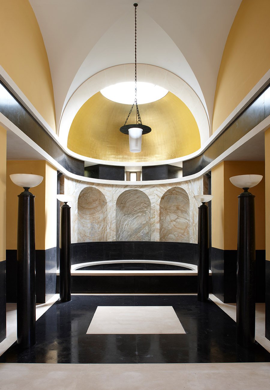 Classical apse interior within a Gloucestershire bath house featuring vaulted ceilings, stone niches and black marble columns.