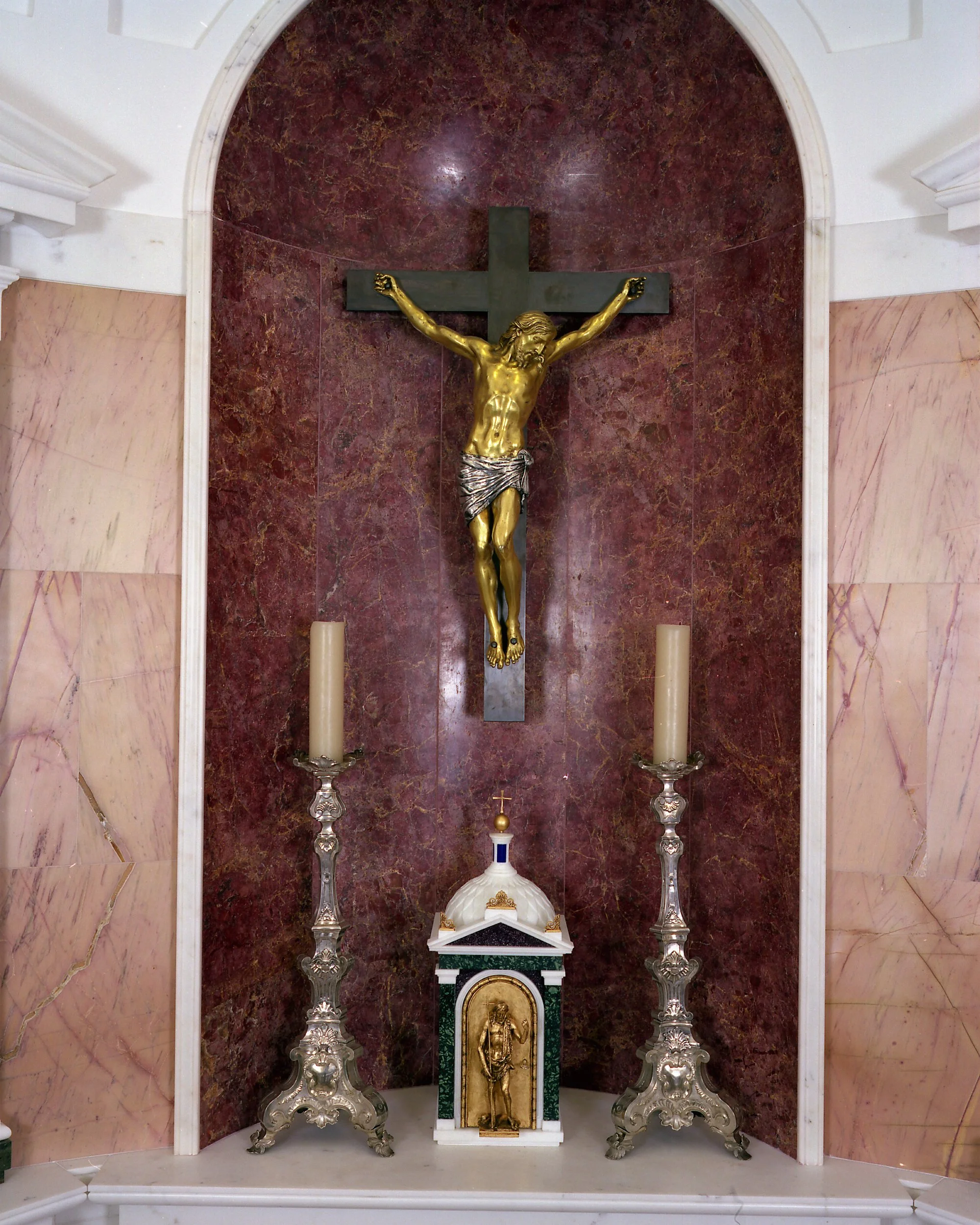 Crucifix above the chapel altar set within a richly detailed stone niche, accompanied by traditional liturgical furnishings.