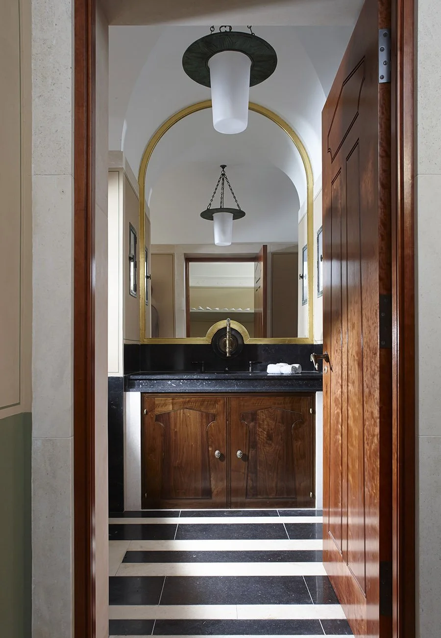 View through a timber doorway into a washroom with classical detailing and marble finishes in the Gloucestershire bath house.