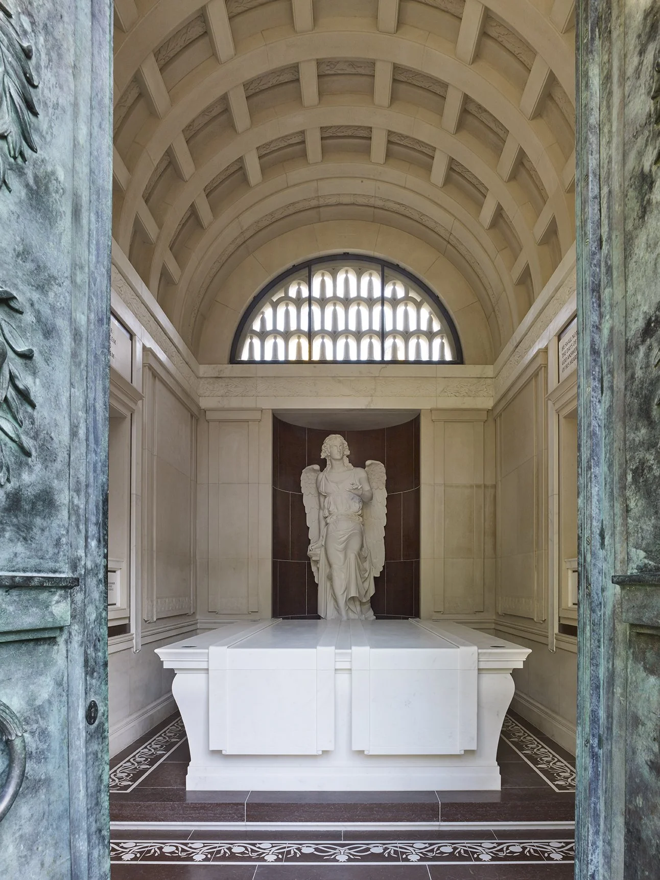 View through the bronze entrance doors into the mausoleum chamber with a coffered stone vault and central memorial sculpture.