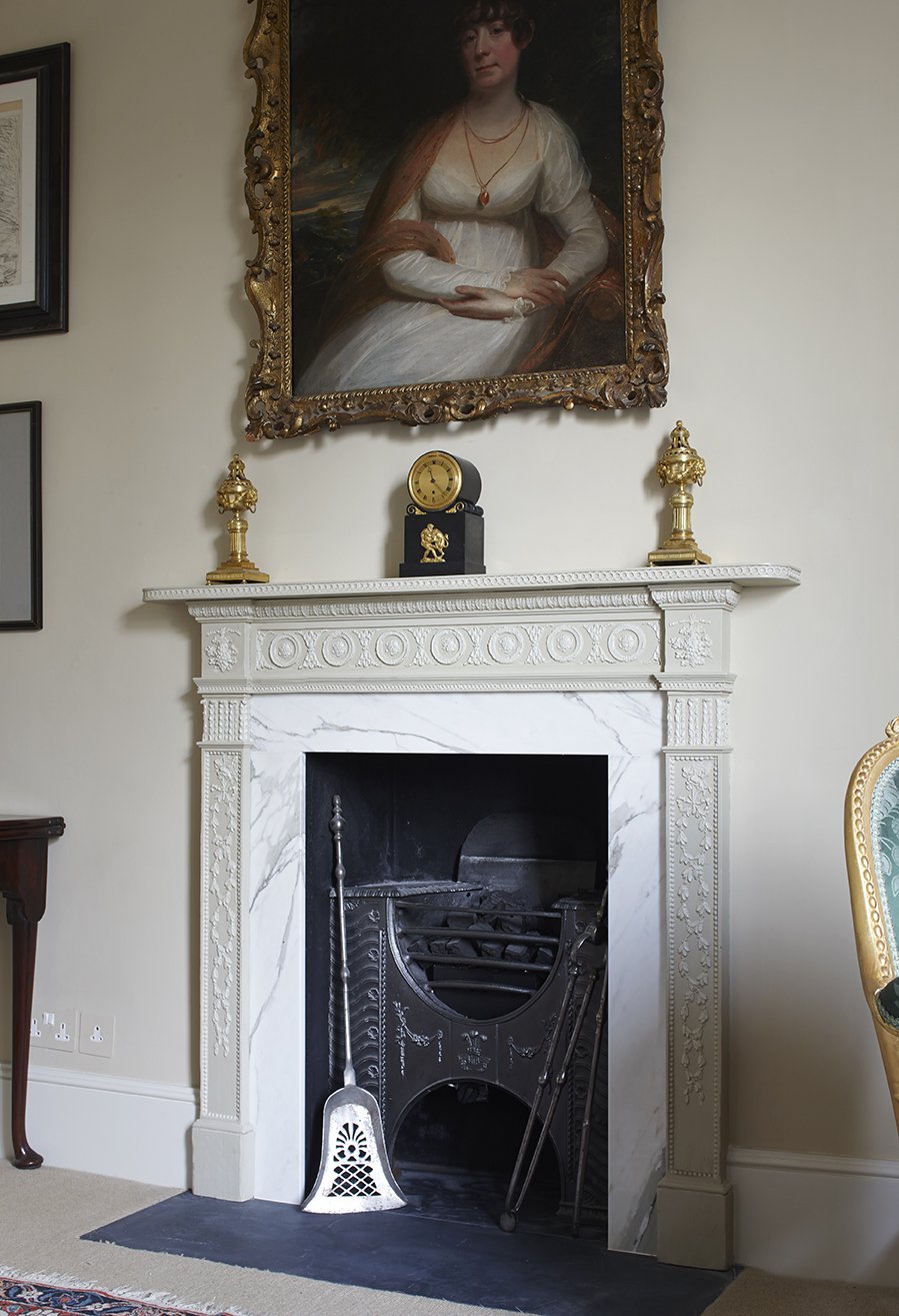 Decorative period fireplace with carved surround and portrait artwork in a historic London apartment.