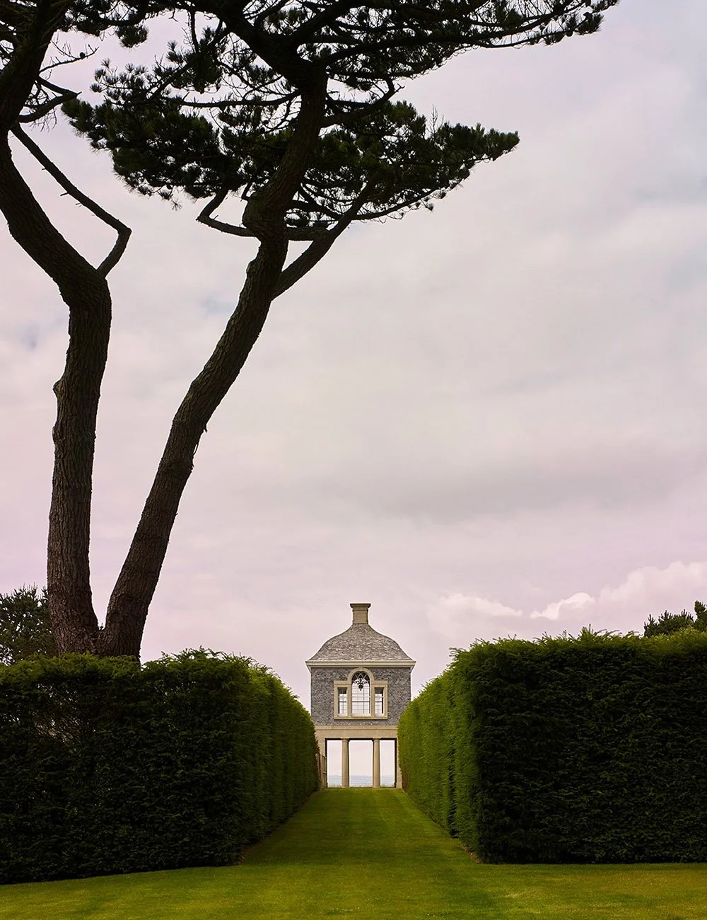 Formal garden avenue in Cornwall leading to a classical pavilion framed by clipped hedges.