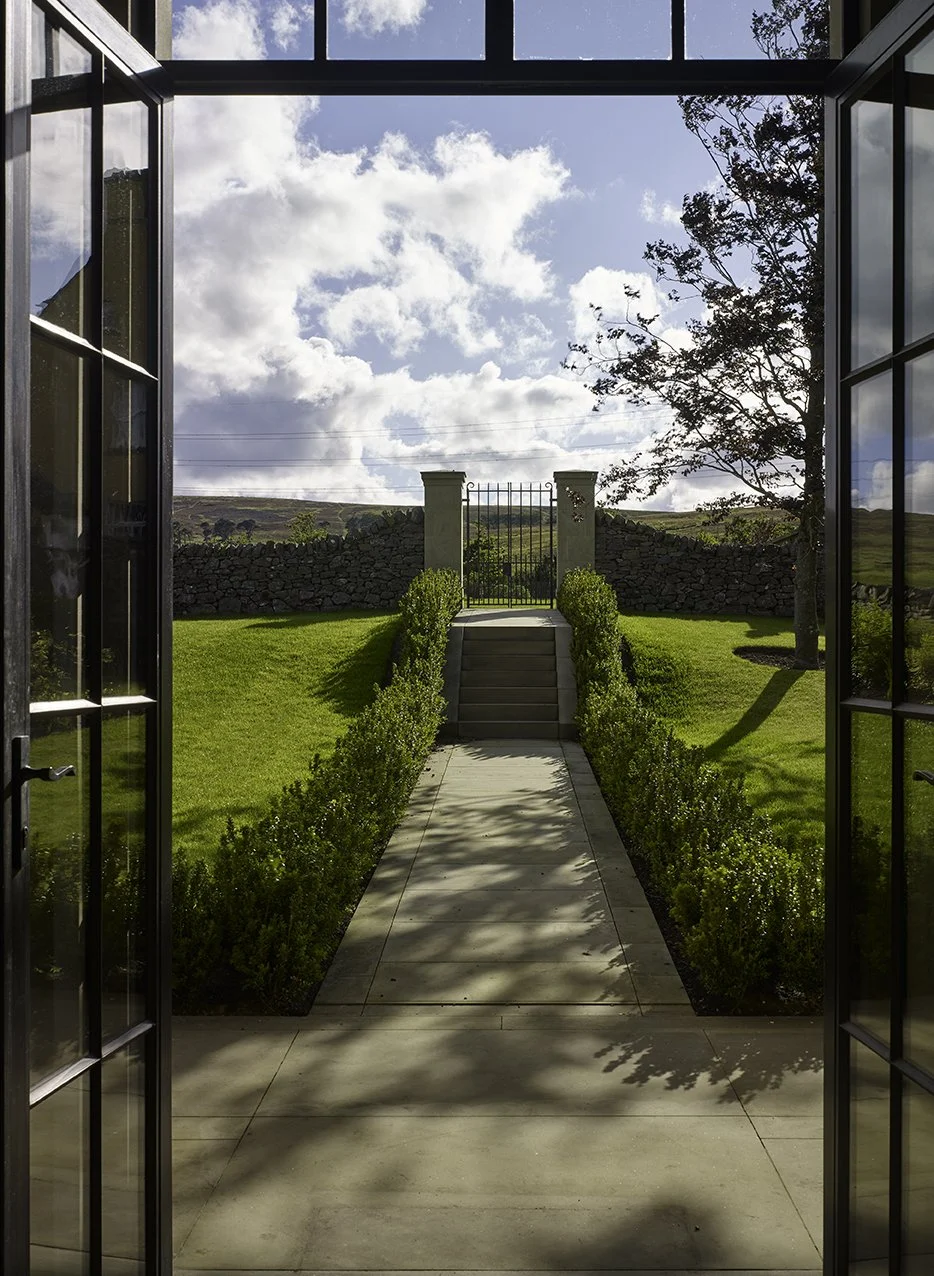 Formal garden walkway and stone steps extending from the orangery towards a garden gate and surrounding landscape.