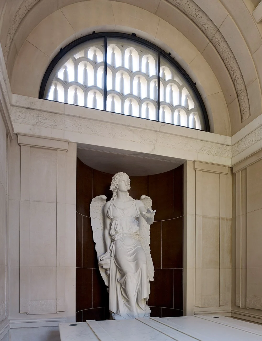Classical angel sculpture within the mausoleum interior beneath an arched clerestory window and coffered vault.