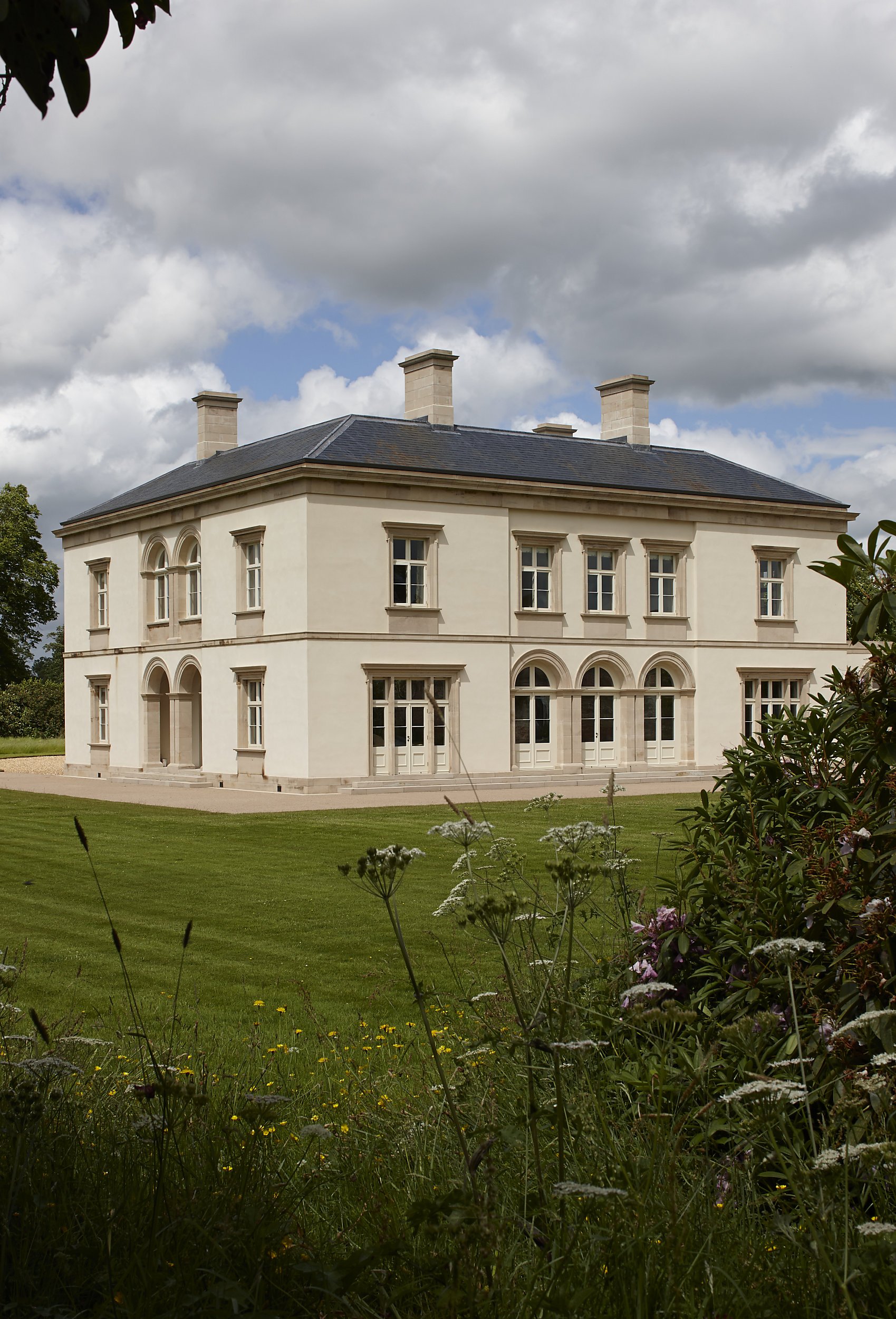 Classical Shropshire country house with symmetrical rendered façade, arched openings and formal lawns viewed through wild garden planting