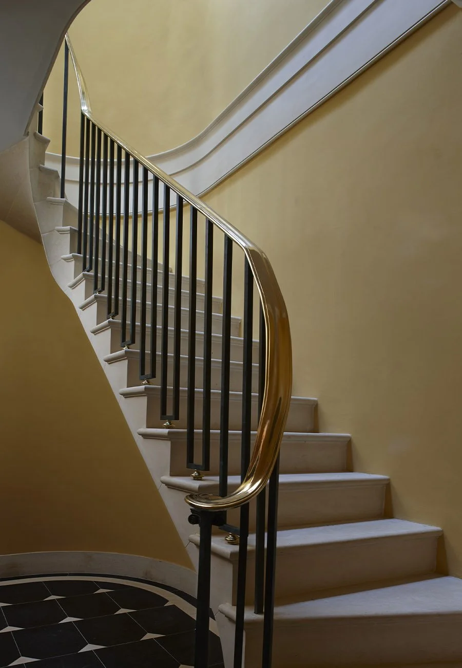 Elegant curved staircase with wrought iron balustrade and classical detailing inside the Gloucestershire bath house.