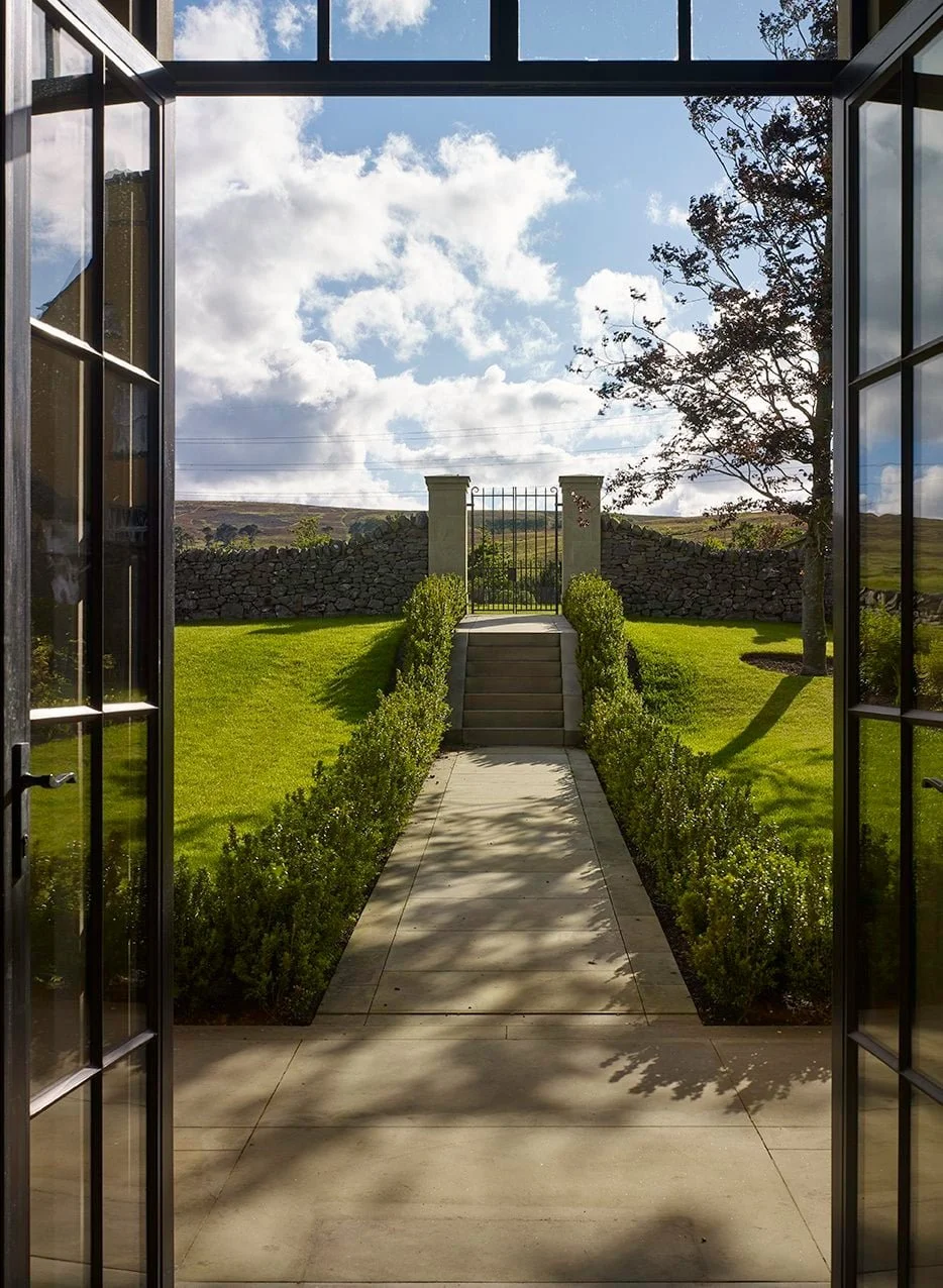 Formal garden walkway and stone steps extending from the orangery towards a garden gate and surrounding landscape.