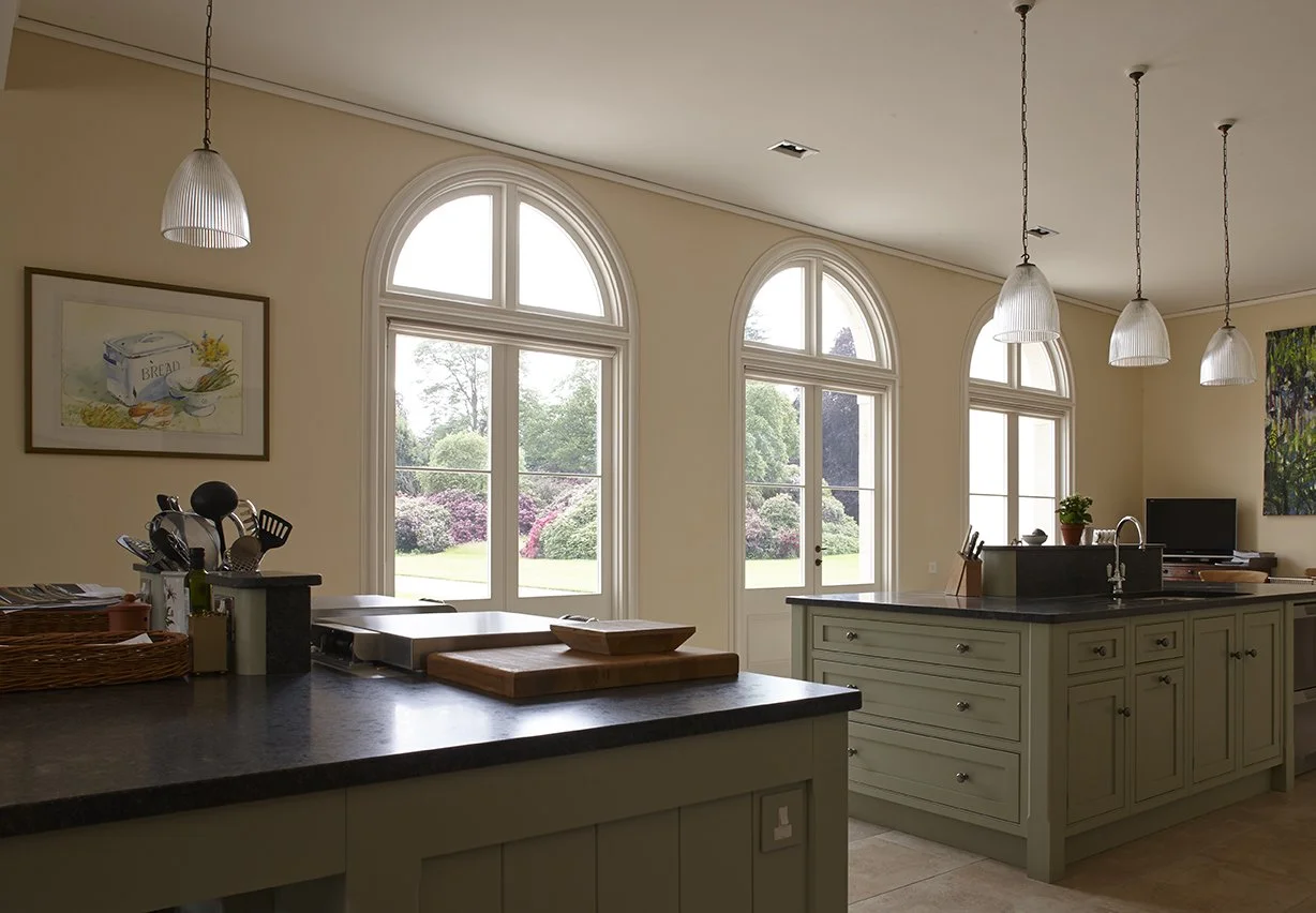 Arched windows illuminating a classical kitchen interior with bespoke cabinetry and garden views