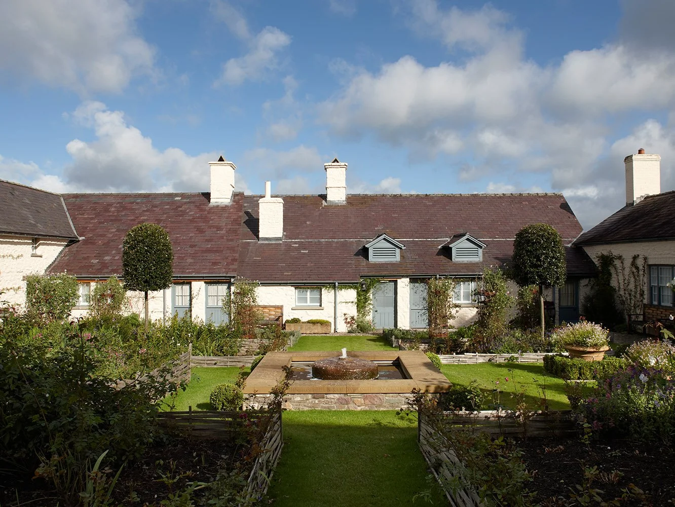 Formal courtyard garden with reflecting pool and restored stone buildings at Llwynwermod, Carmarthenshire.