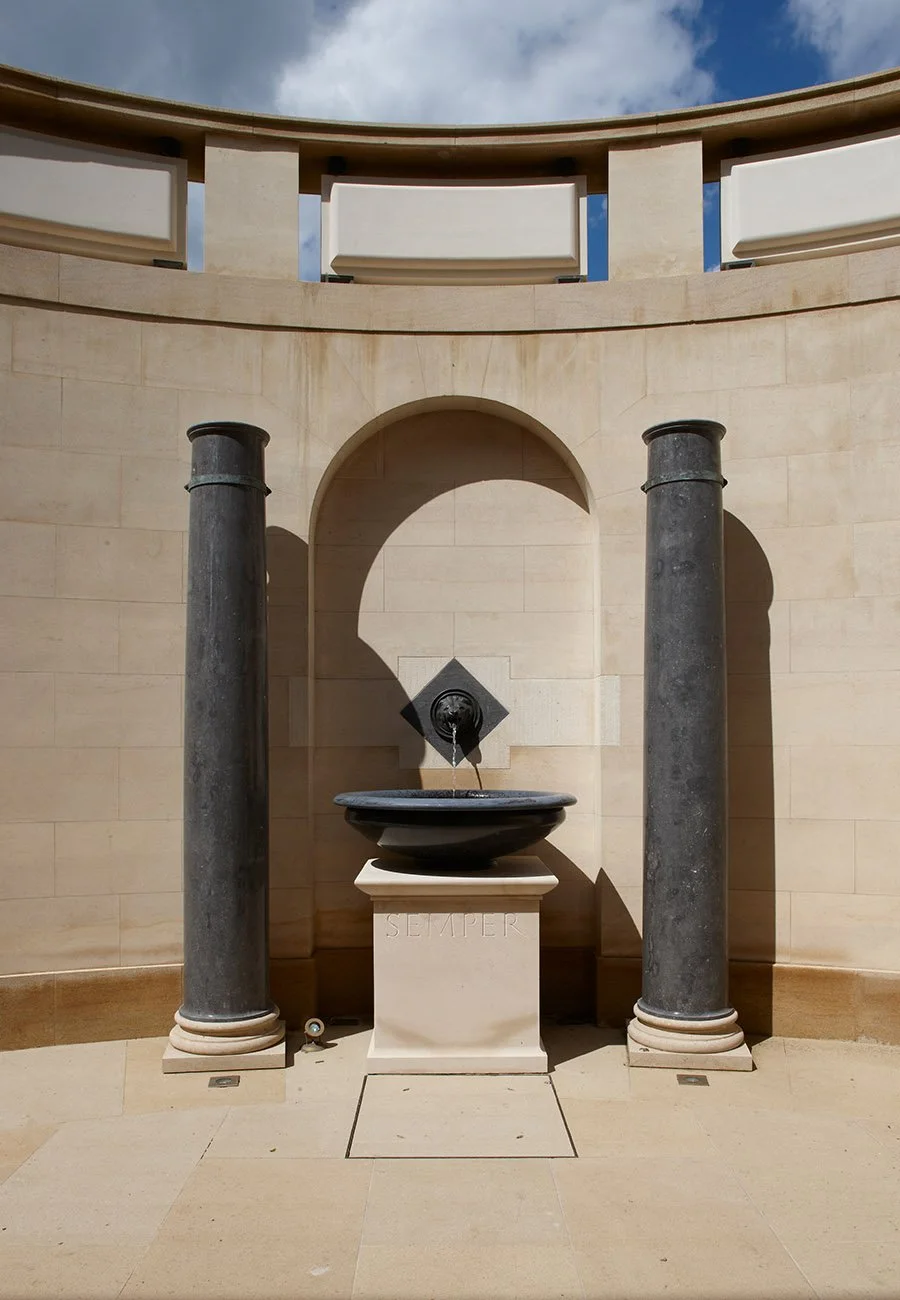 Stone fountain set within a classical niche framed by dark marble columns inside the Gloucestershire bath house.