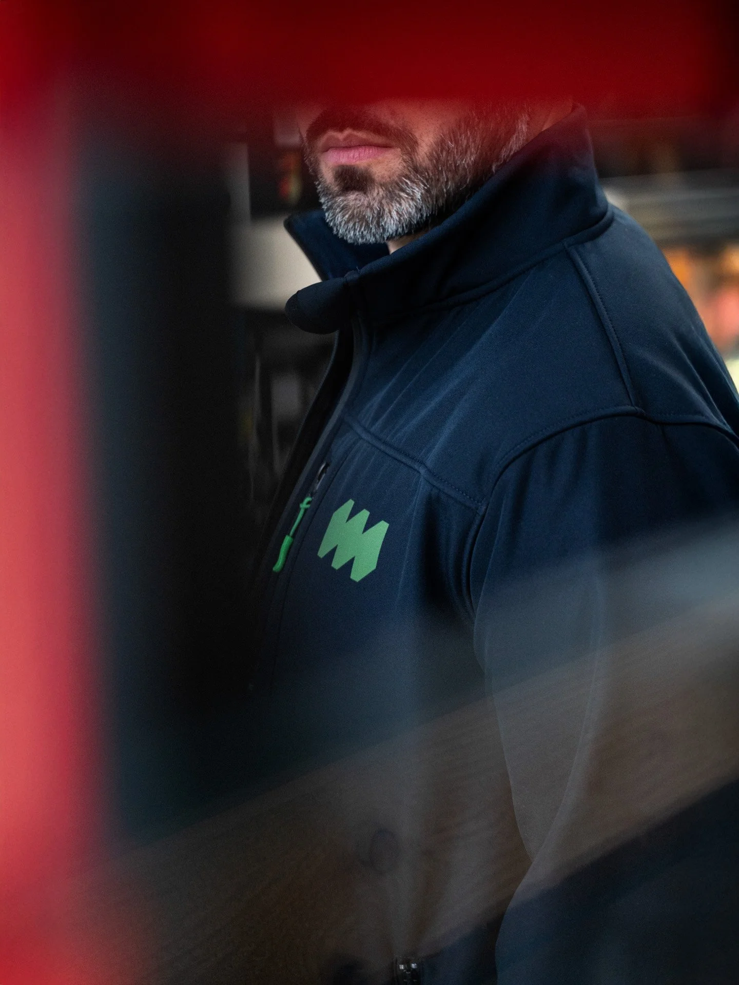 Nahaufnahme eines Mannes in dunklem Mantel, nur der Bart und die Lippen sind sichtbar, im Hintergrund unscharf, wahrscheinlich in einer urbanen Umgebung.