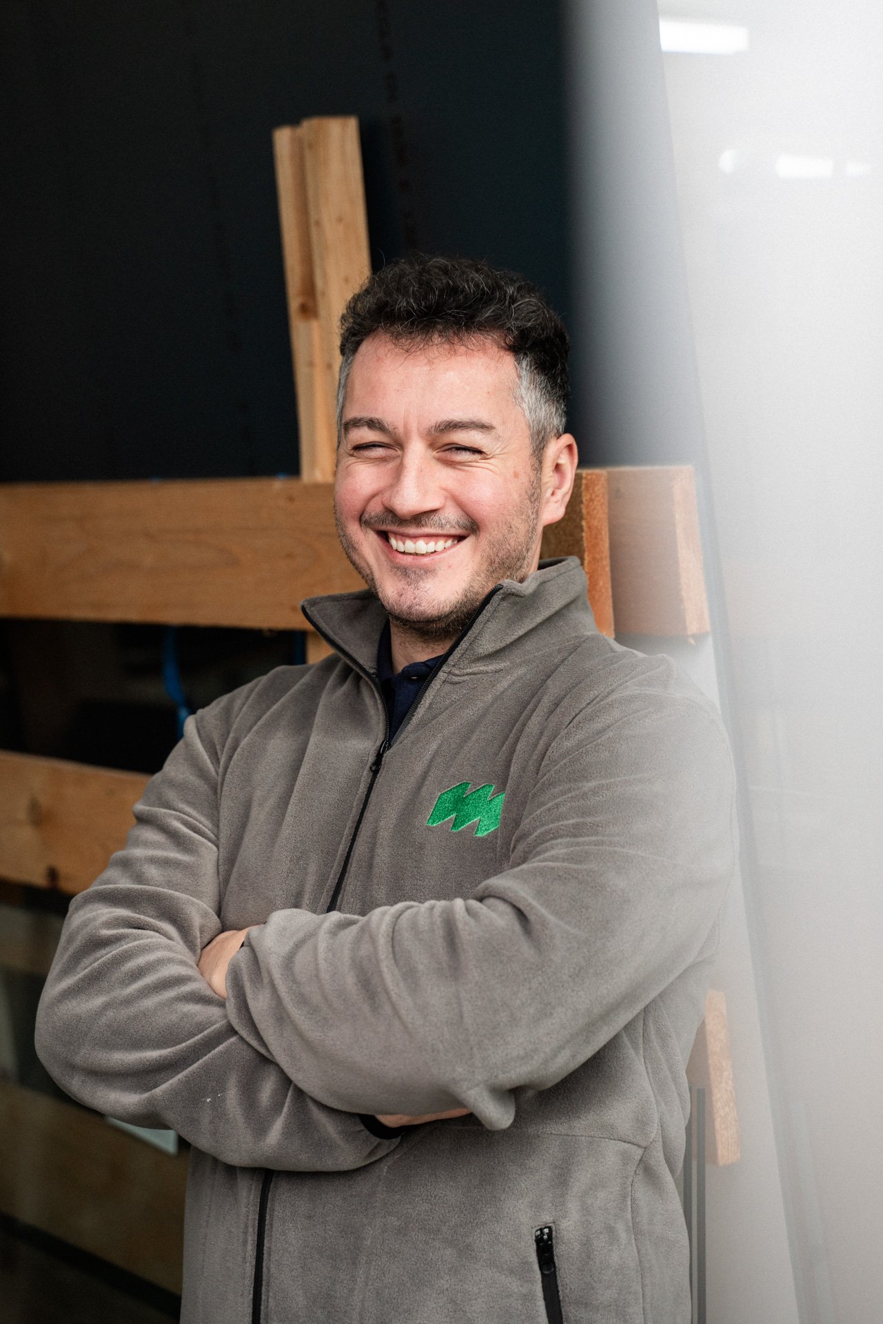 Mann lächelt in Kamera und trägt dabei eine Fleecejacke in einer Werkstatt 