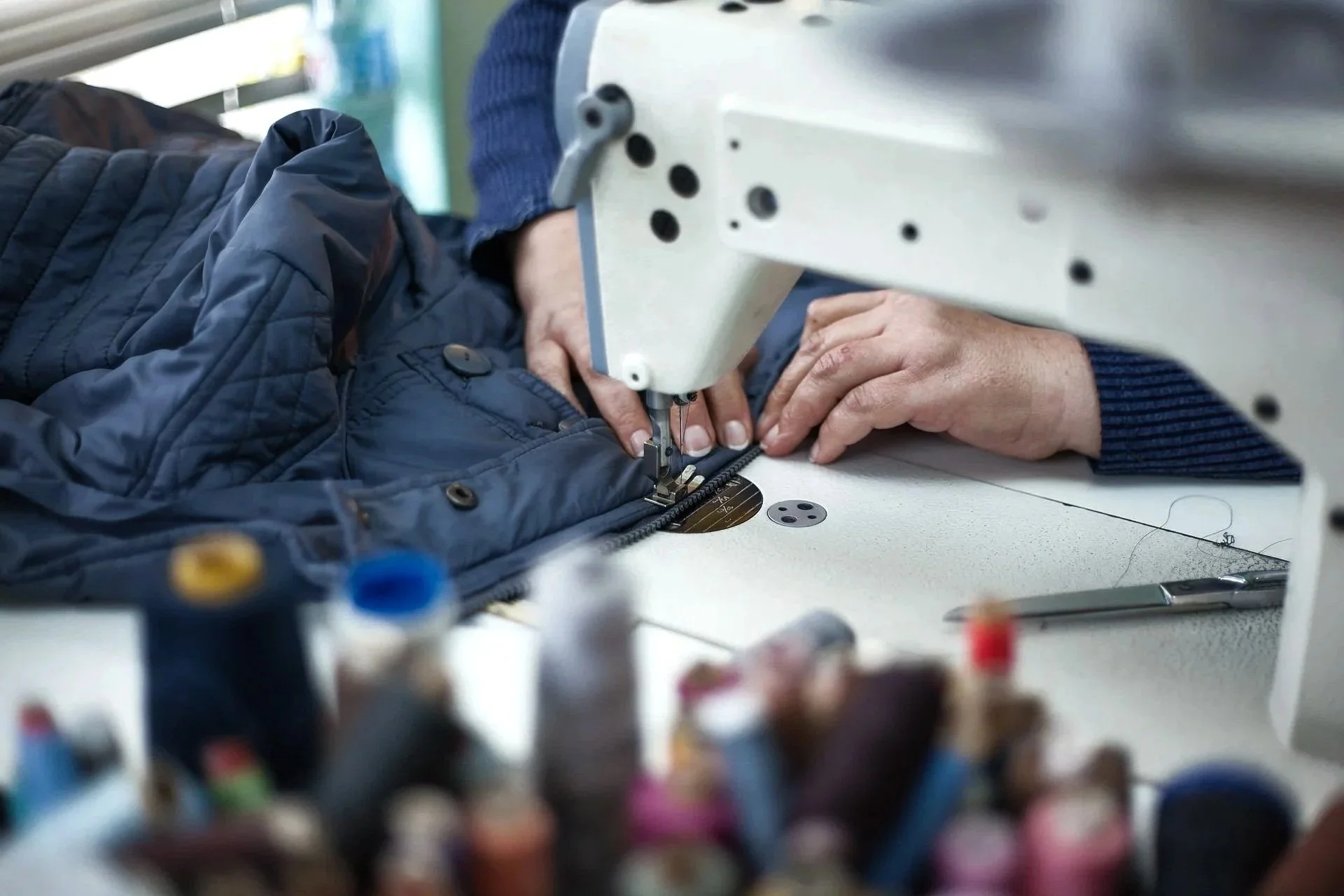 Person näht eine schwarze Jacke an einer Nähmaschine in einer Werkstatt.