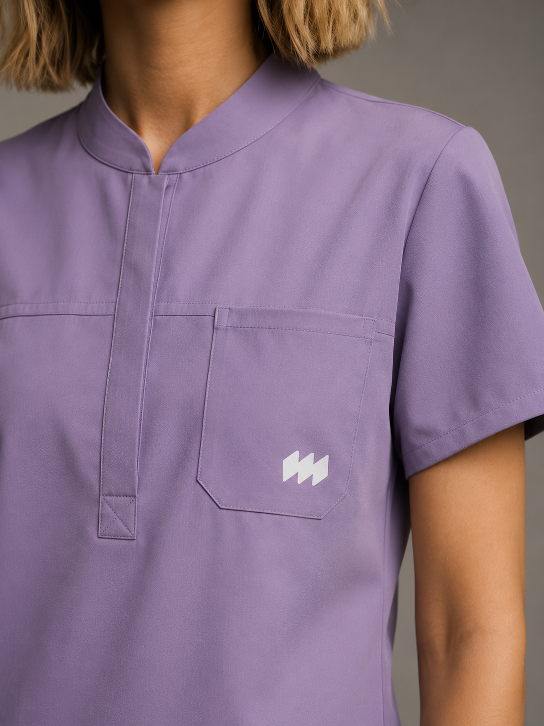 Nahaufnahme einer Person in lilafarbener medizinischer Uniform mit Brusttasche und Logo auf der Tasche