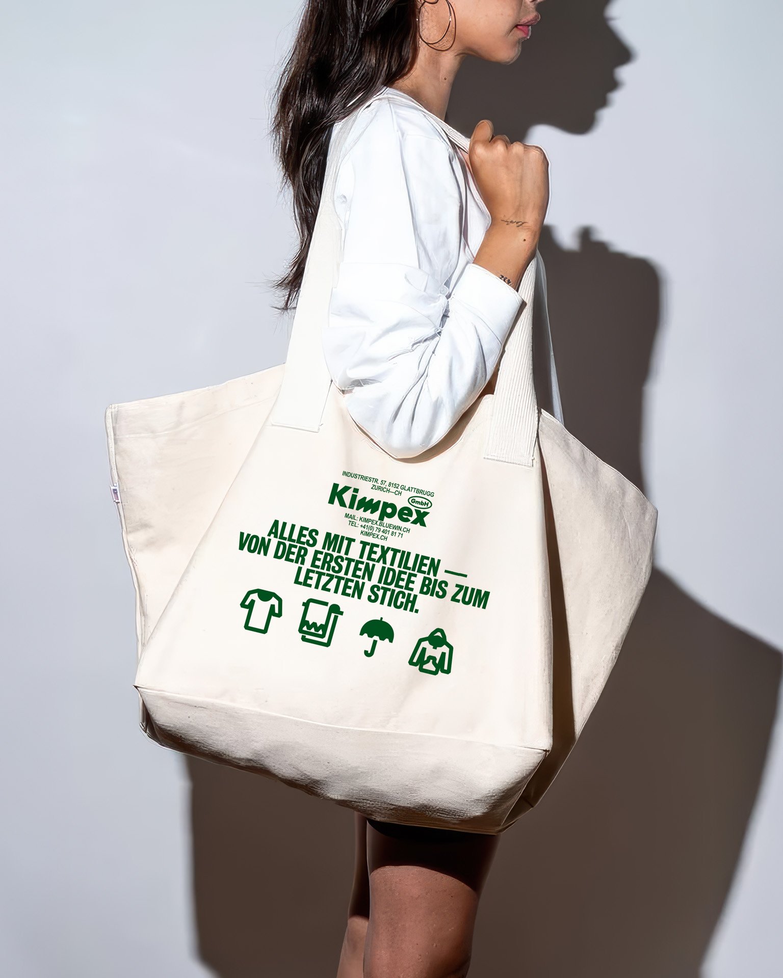 Eine Frau mit dunklem Haar trägt einen großen weißen Stoffbeutel mit grüner Aufschrift zum Thema Textilrecycling.