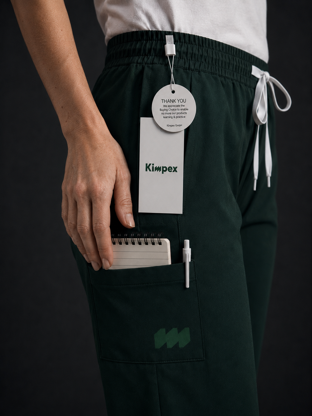 Person trägt schwarze Hosen mit Aufdrucken, hält einen kleinen Notizblock und hat ein Namensschild mit der Aufschrift 'Kimpex' an der Tasche befestigt.