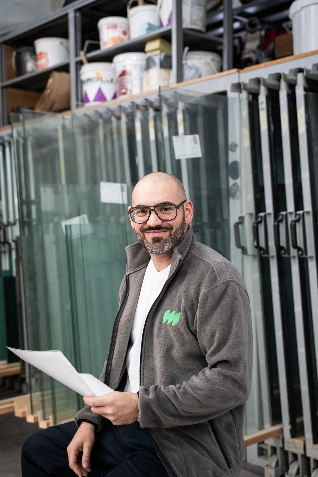 Mann trägt eine Fleecejacke, hält ein Blatt Papier in der Hand, in einem Atelier