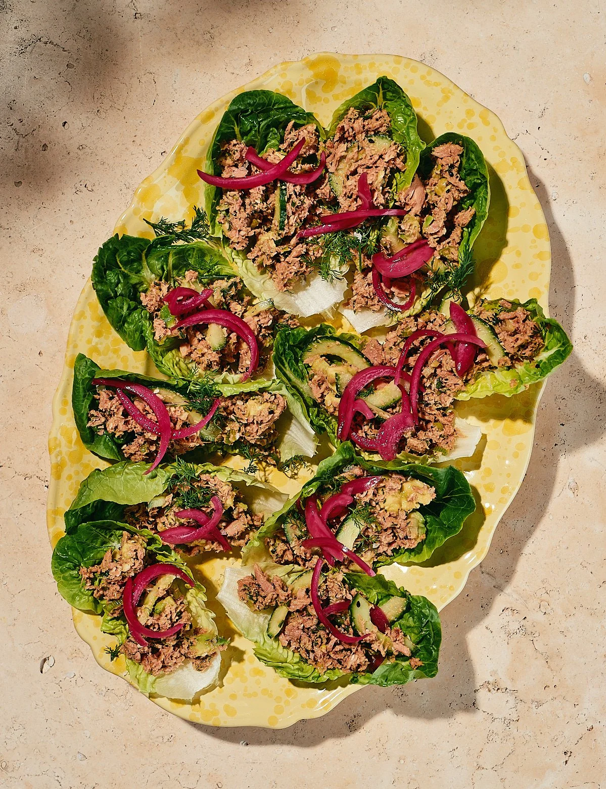 Lettuce wraps with ground meat and pickled red onions on a yellow platter.