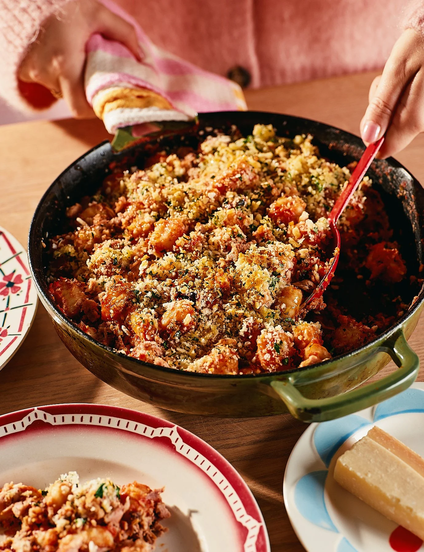A baking dish filled with stuffing next to a plate with a serving of stuffing and a small plate with a piece of cornbread.
