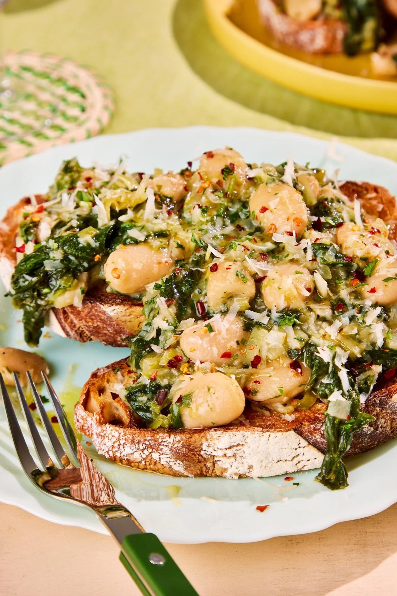 Toasted rustic bread topped with a mixture of green leafy vegetables, scallops, and shredded cheese, served on a white plate.