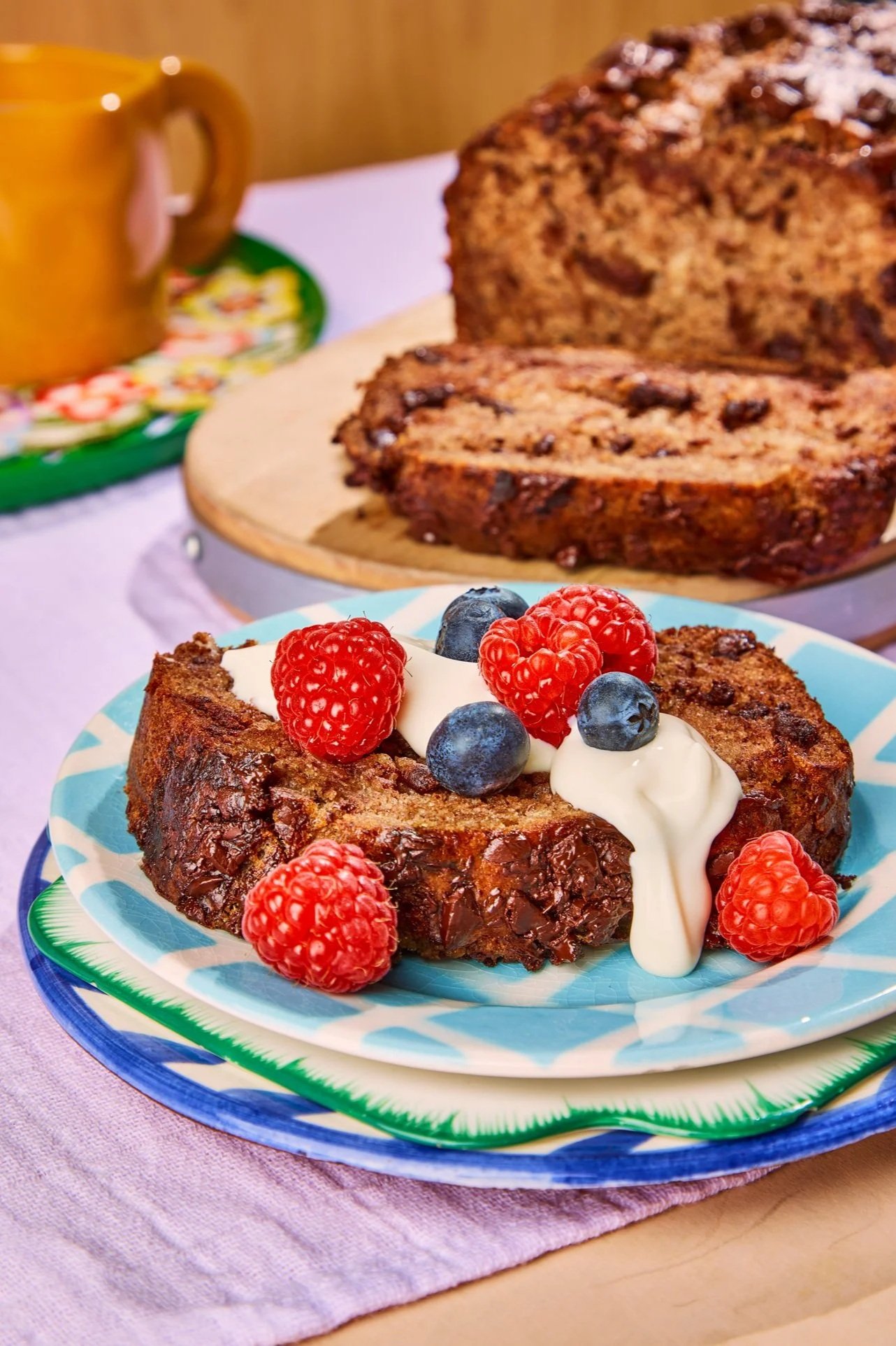 Slice of fruitcake topped with whipped cream, raspberries, and blueberries, served on a decorative plate.