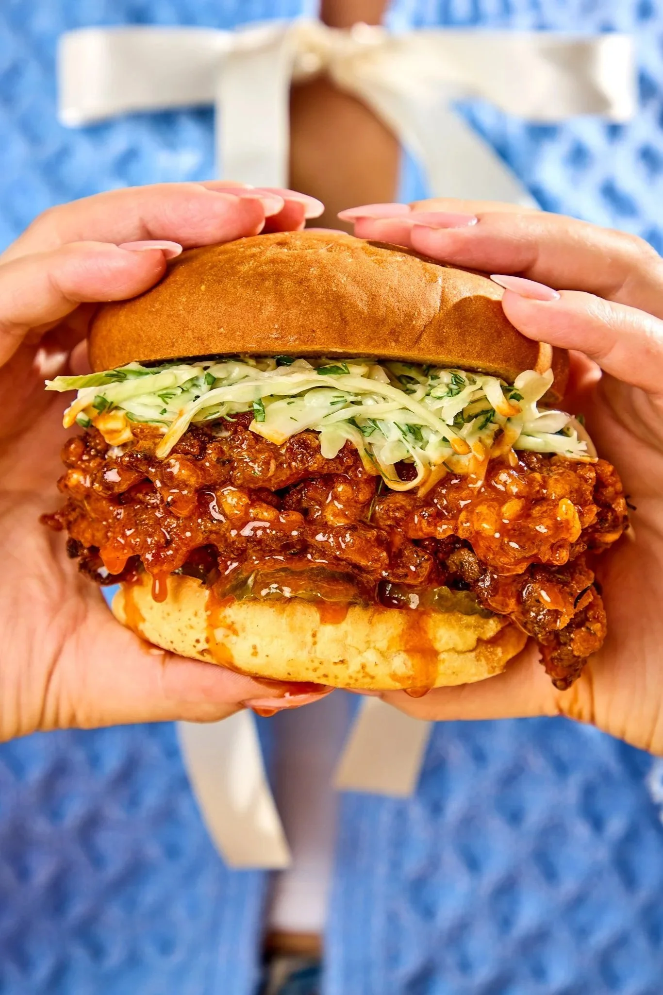 Person holding a spicy meat-filled sandwich with shredded lettuce, wrapped in a sandwich bun.