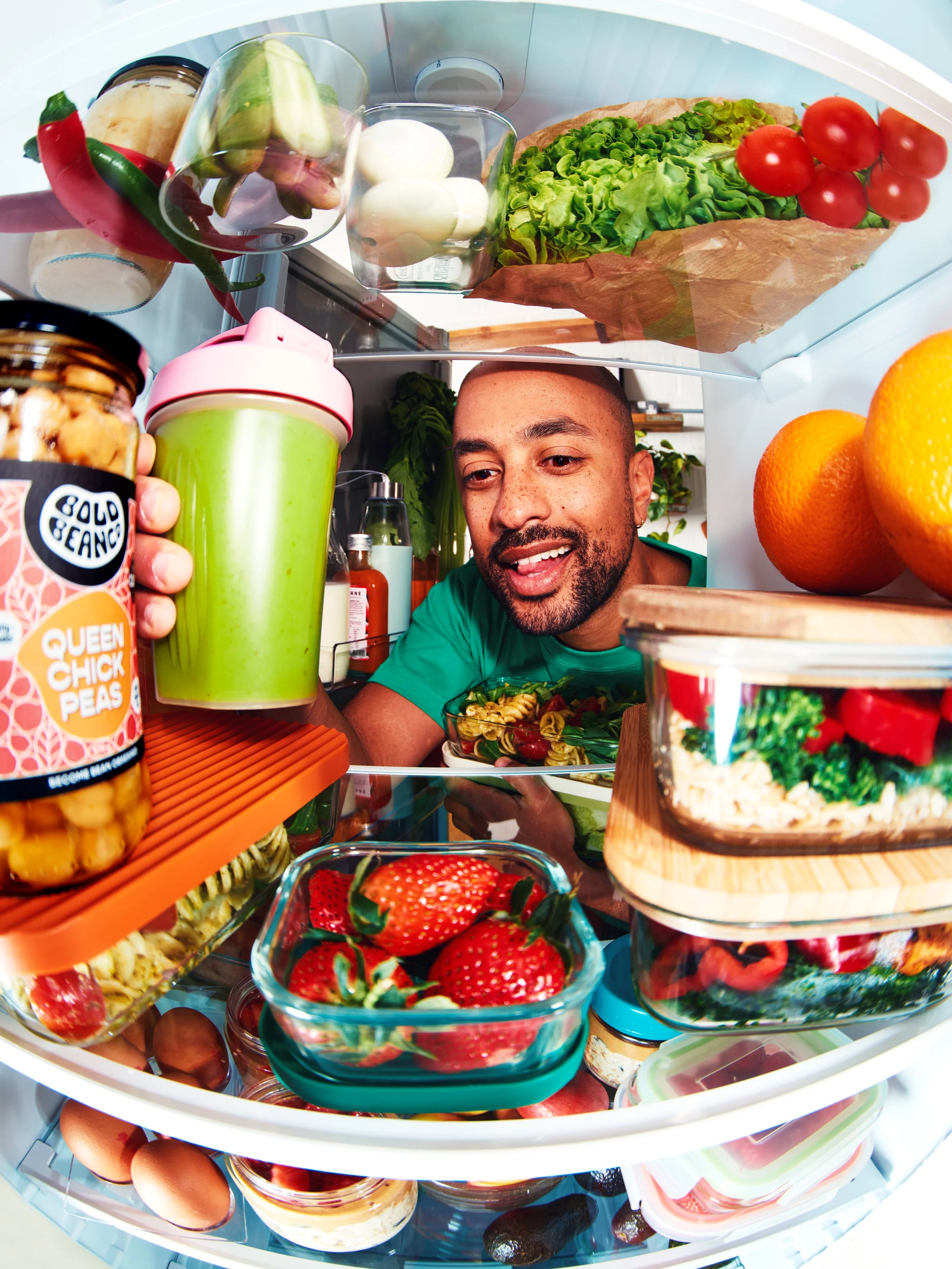The inside of a refrigerator door filled with various food items including strawberries, eggs, jars of spreads, a green smoothie, cherry tomatoes, a loaf of bread, a bowl of salad, and containers of other food items.