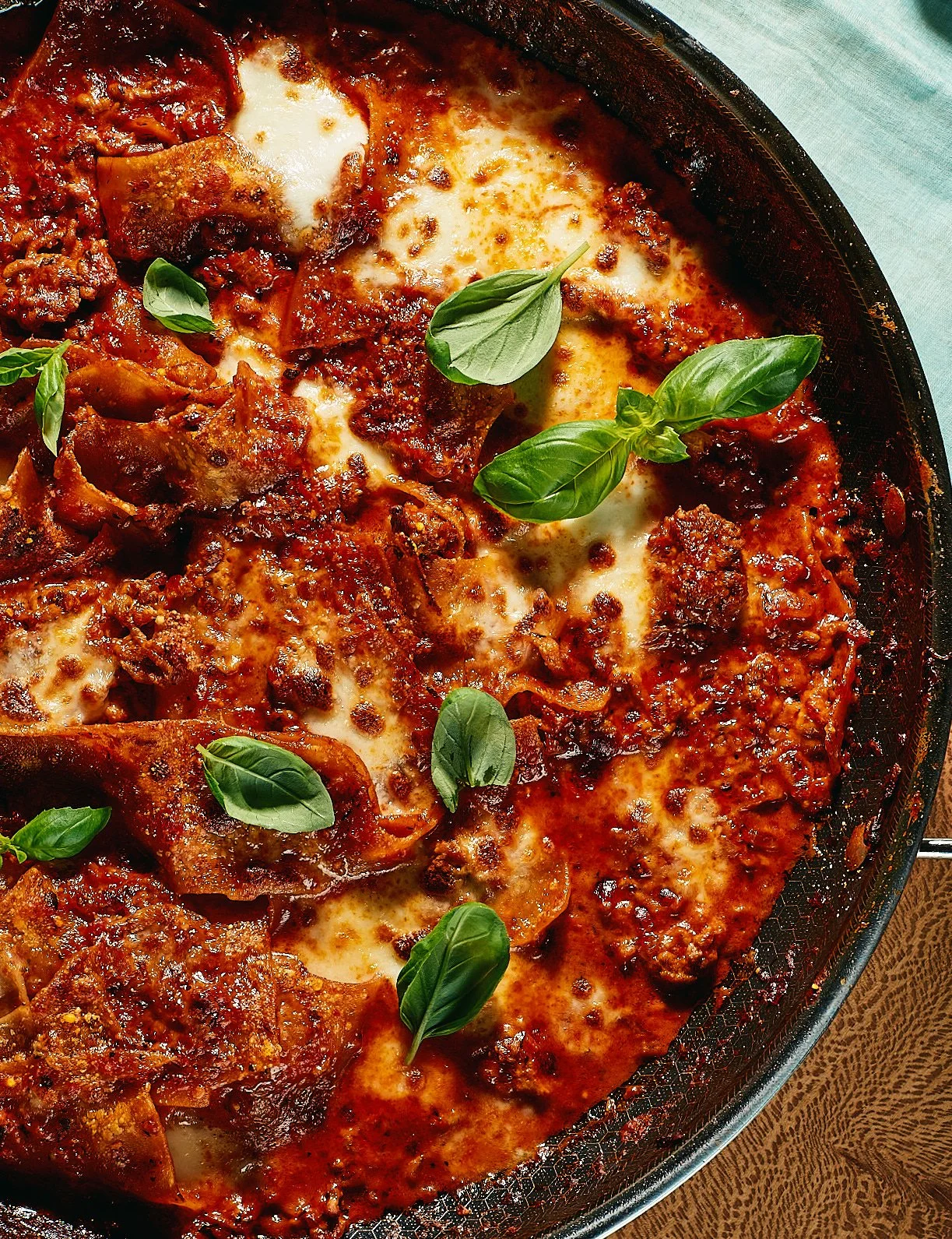 Baked lasagna with melted cheese, meat sauce, and fresh basil garnish, served in a black baking dish.