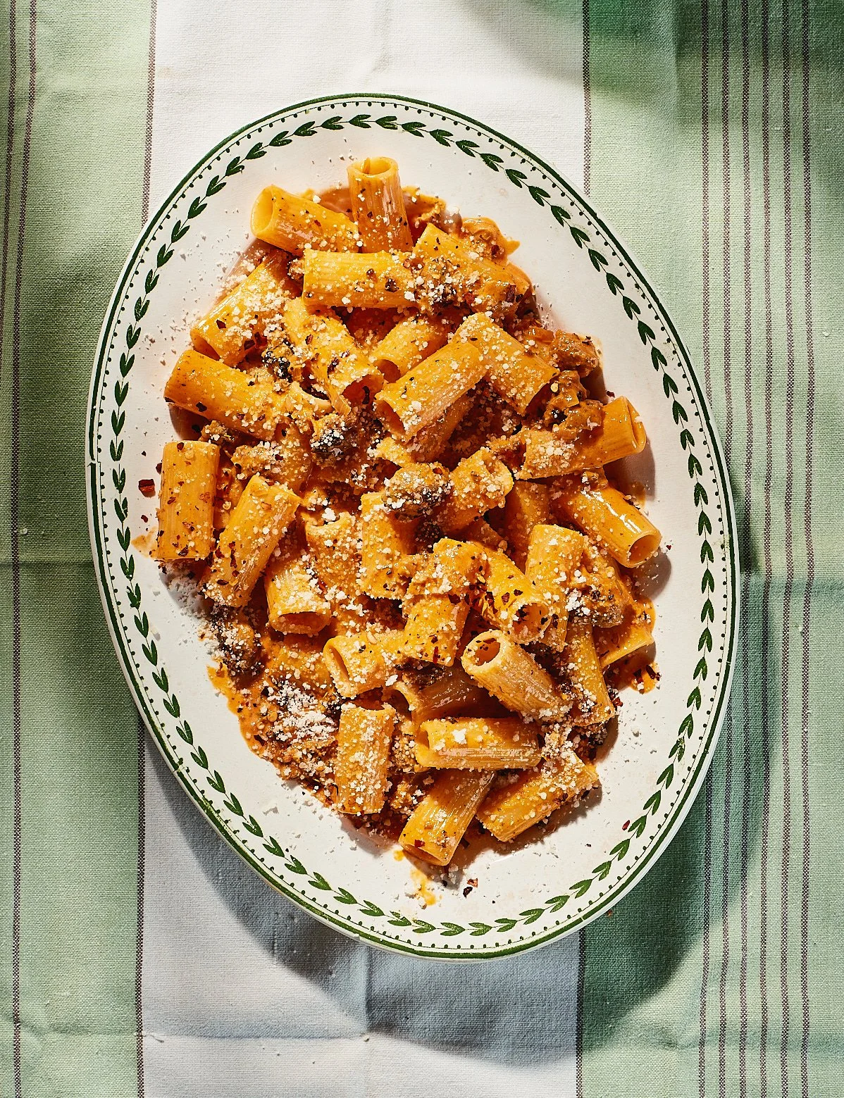 Plate of cooked pasta with a tomato-based sauce, topped with grated cheese, on a striped green and white tablecloth.