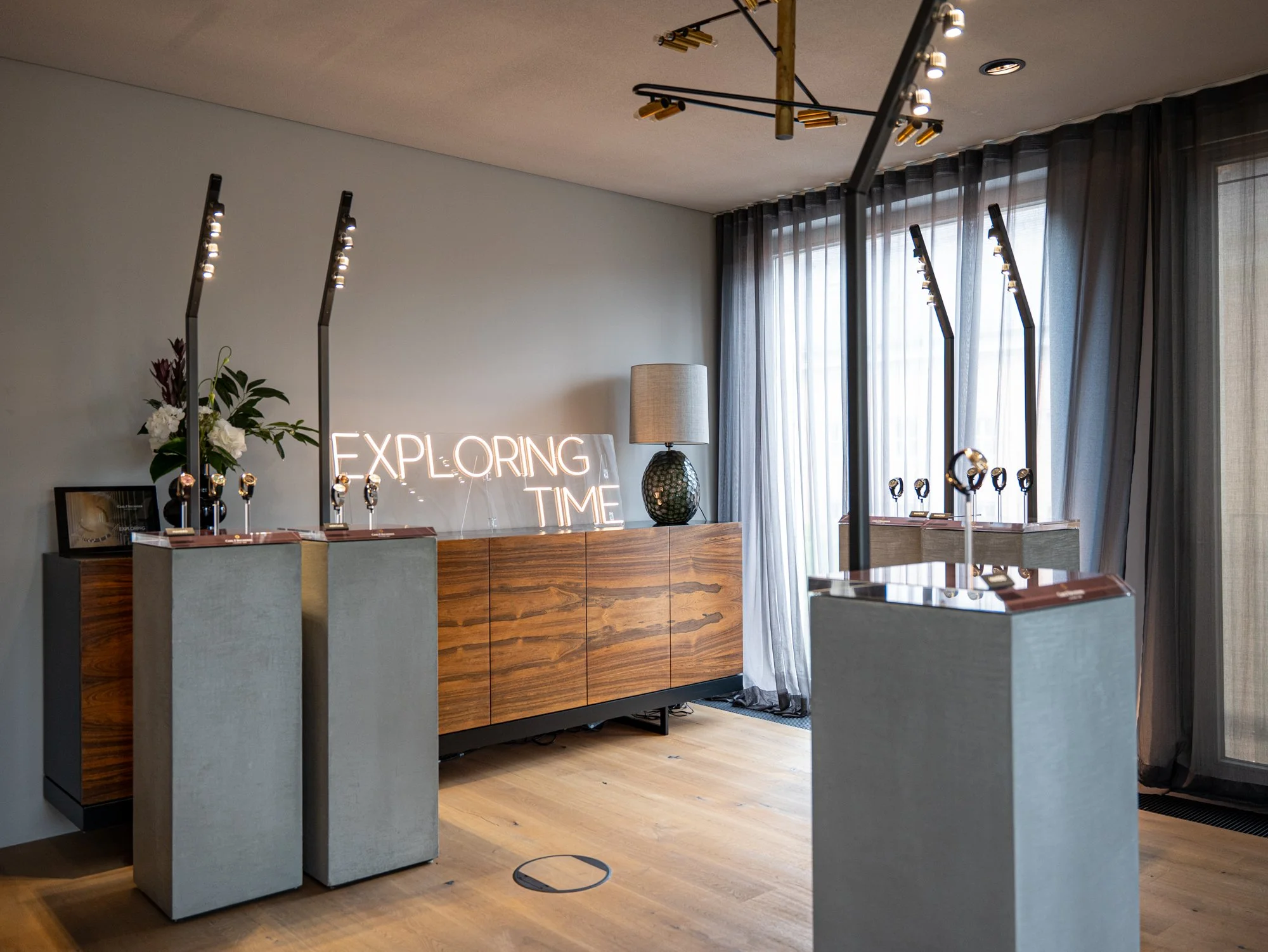 Luxury watch display room with modern decor, featuring illuminated "Exploring Time" sign, watches on pedestals, and stylish lighting fixtures for a luxury watch presentation and media event in Munich.