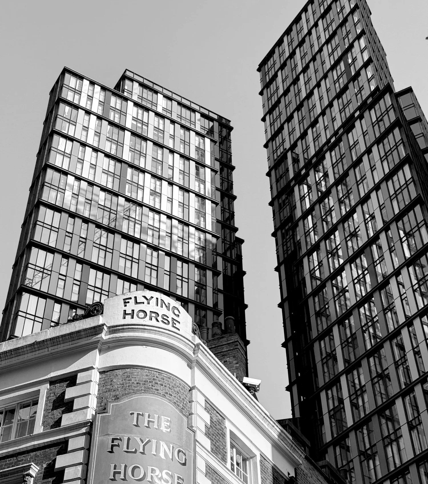 The Flying Horse pub in London with modern residential towers behind, in black and white