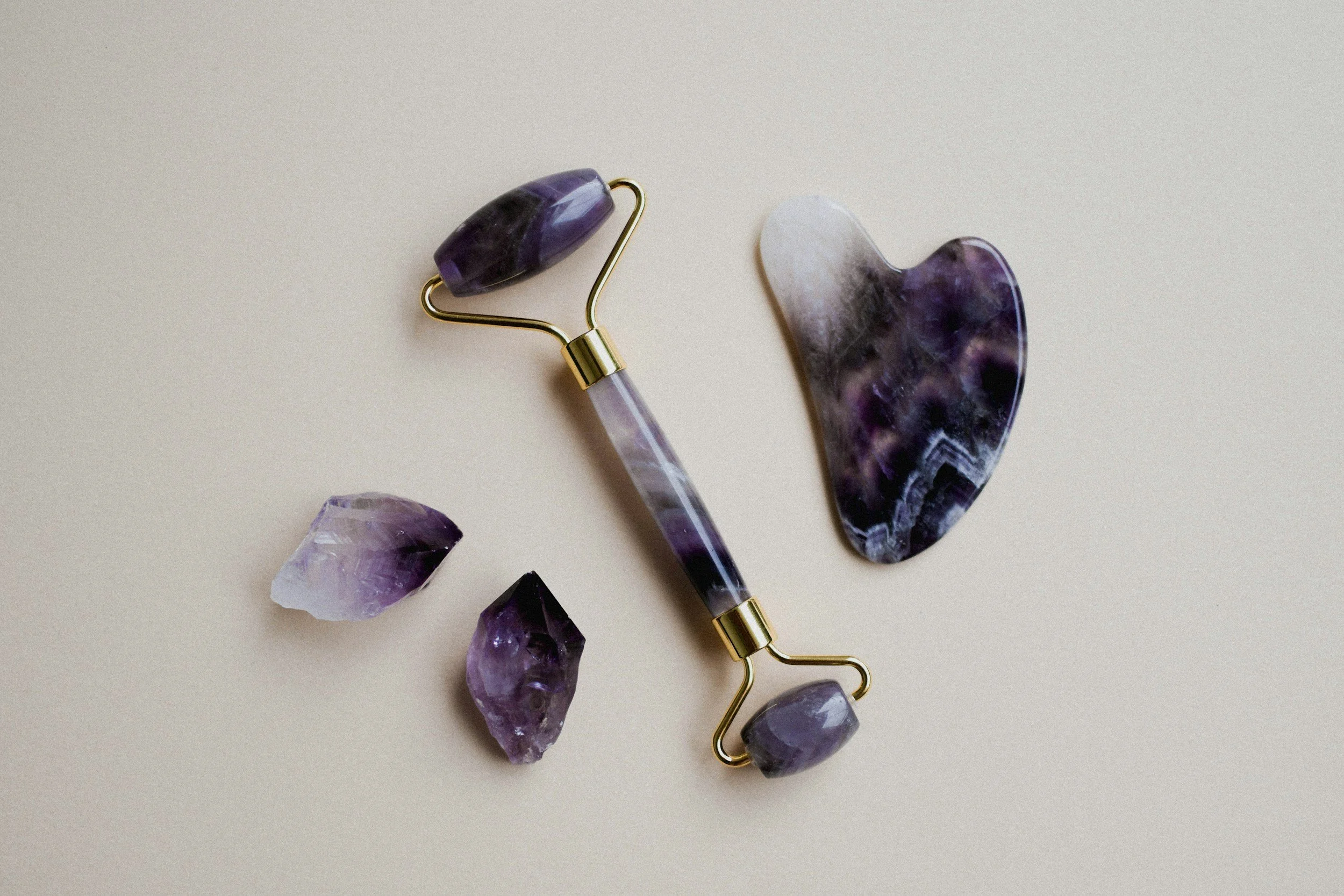 A purple jade roller and two purple gemstones on a white surface.
