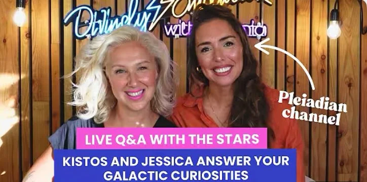 Woman with long hair in a patterned shawl stands against a pastel abstract background with light bokeh effects.