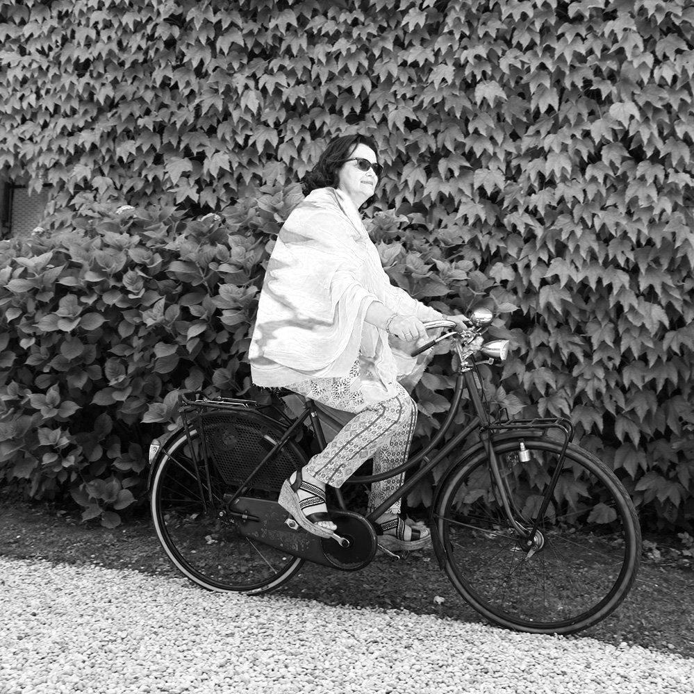 Una donna che pedala su una bicicletta davanti a una parete di foglie.