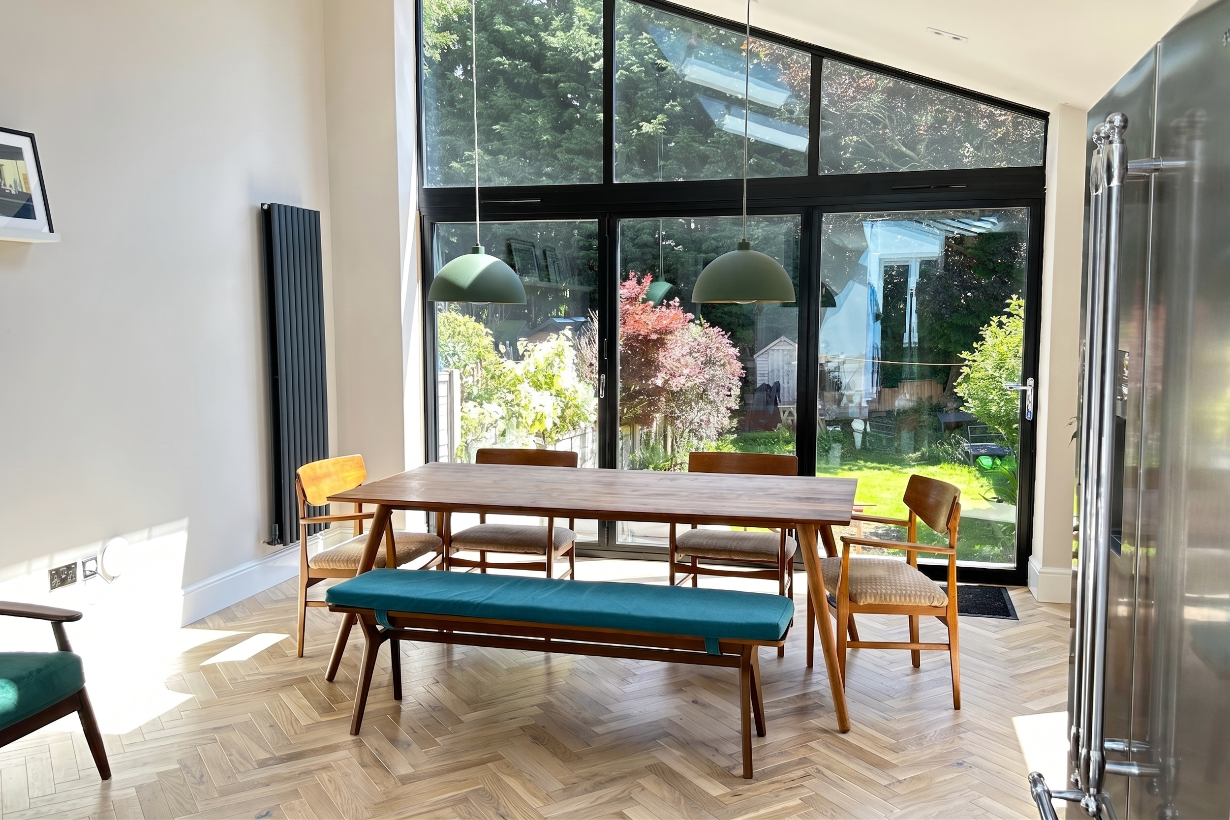 Open-plan kitchen-diner in Birmingham with dining table and bench framed by floor-to-ceiling glazing and garden views