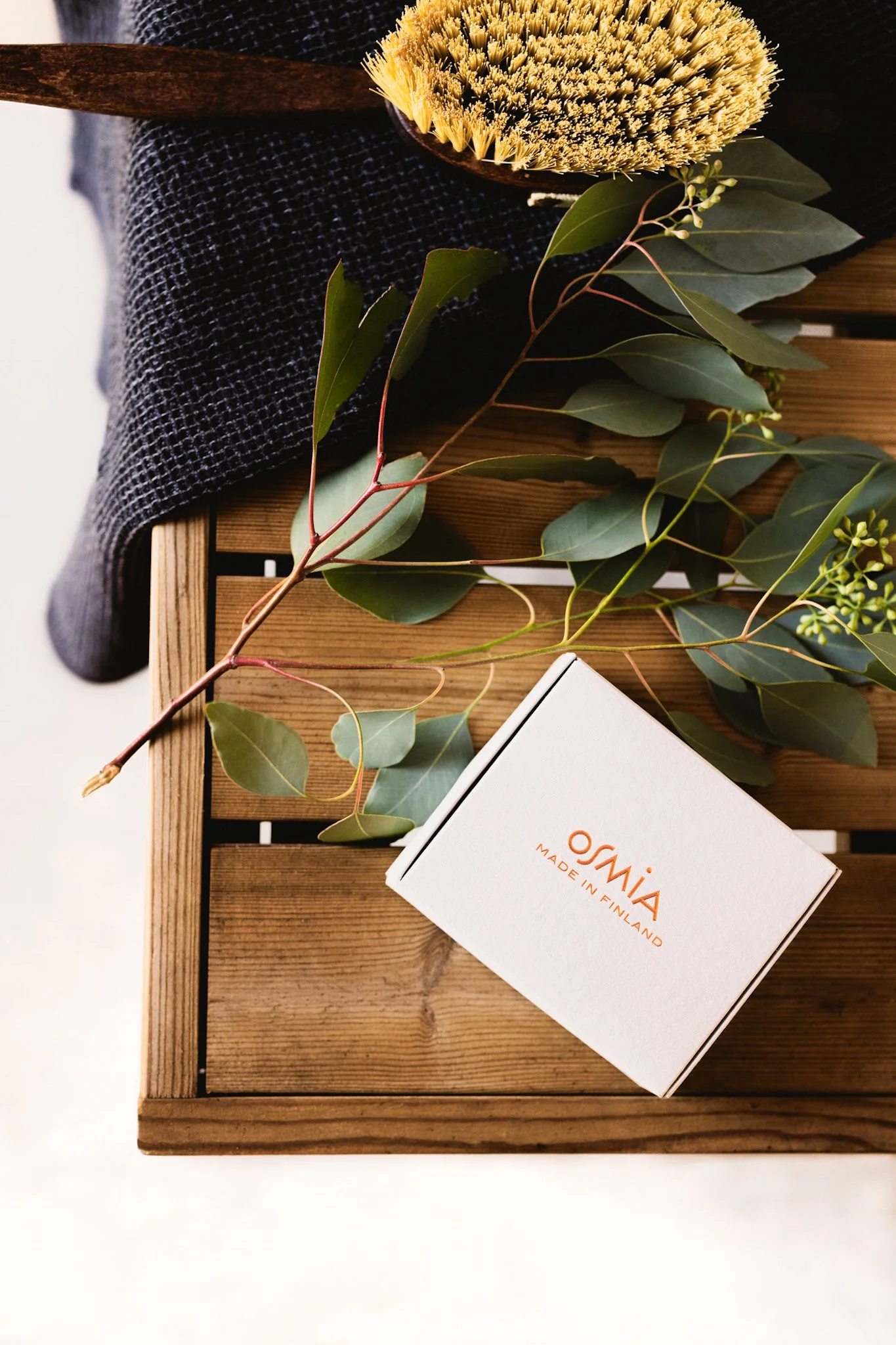 A wooden tray with a black textured cloth, green leaves, and a small white box labeled 'Osmia, Made in Finland'.