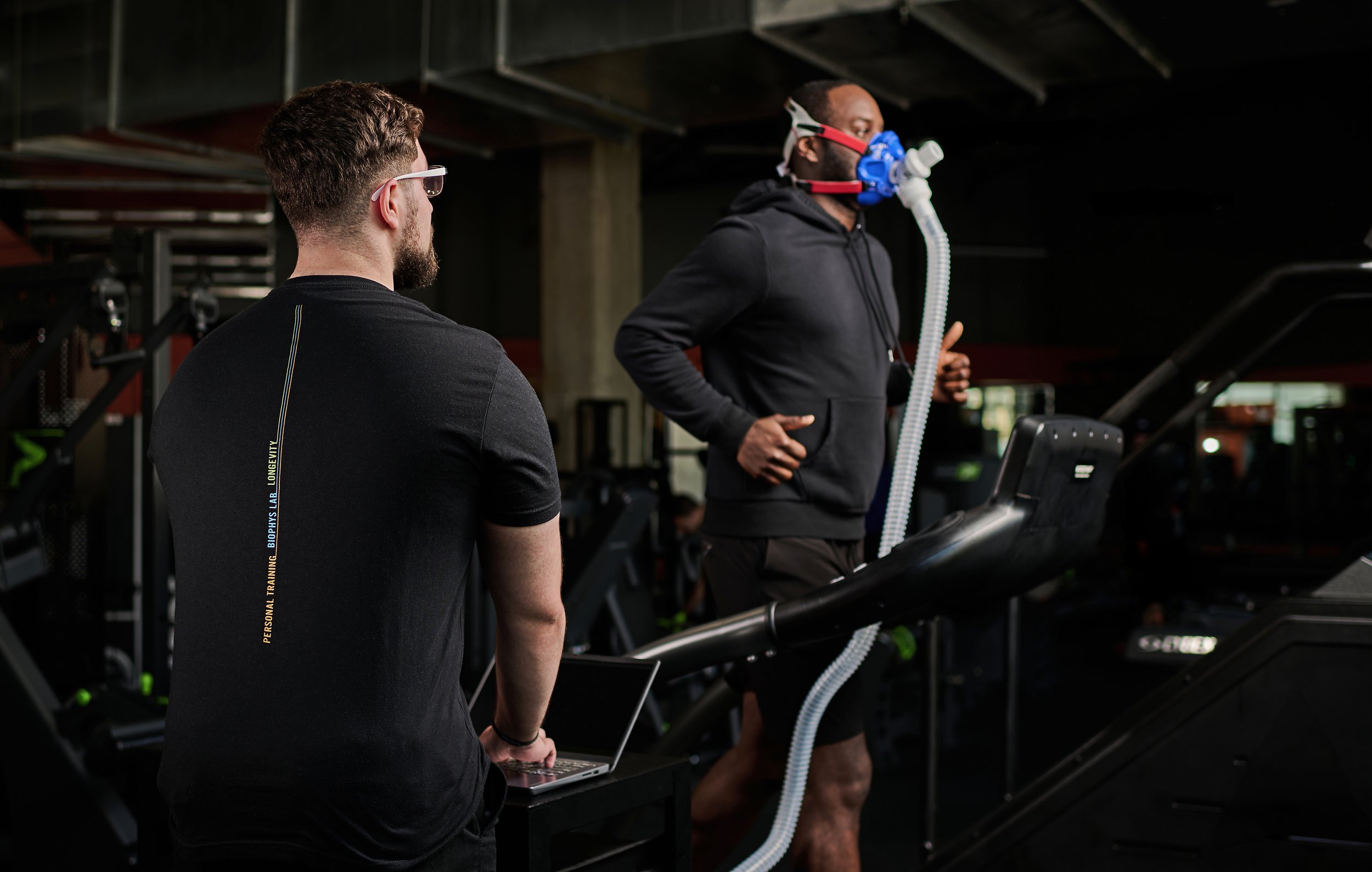 A man wearing a mask on a stationary bike for a fitness or VO2 max test in a lab setting with a computer nearby.