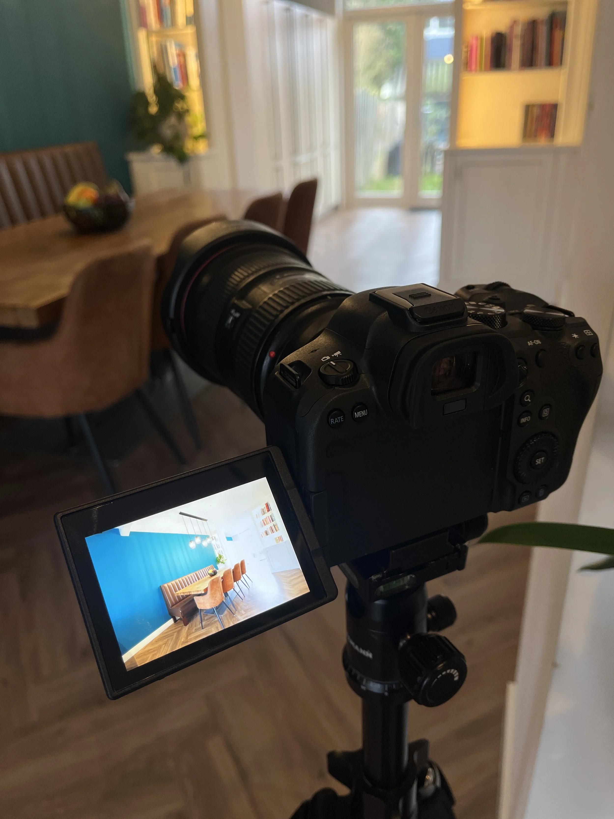 Een professionele camera op een statief, gericht op een interieur met een eethoek en een felle blauwe muur.