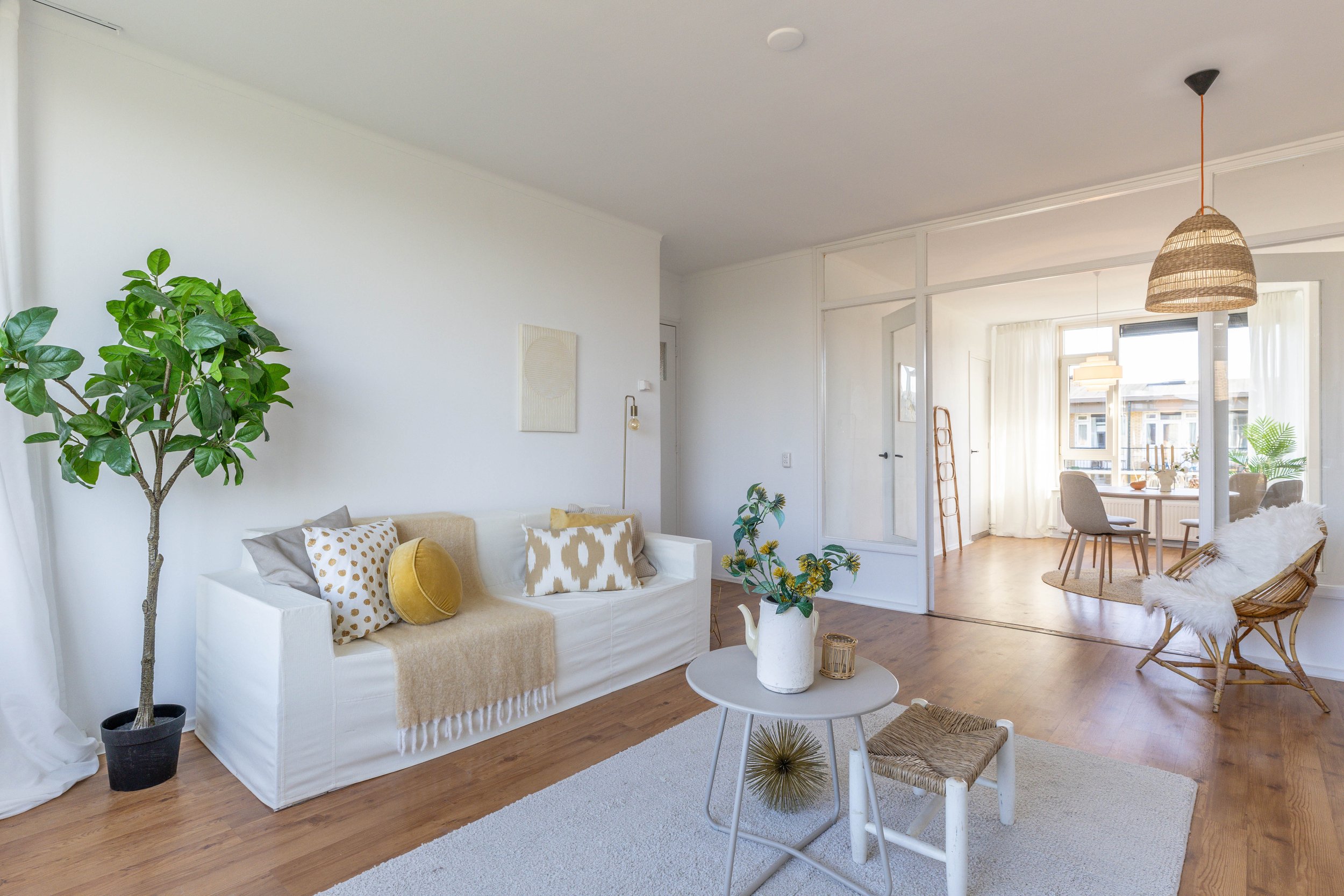 Woonkamer met witte bank, planten, houten vloer, ronde salontafel en veel natuurlijk licht in een modern interieur.