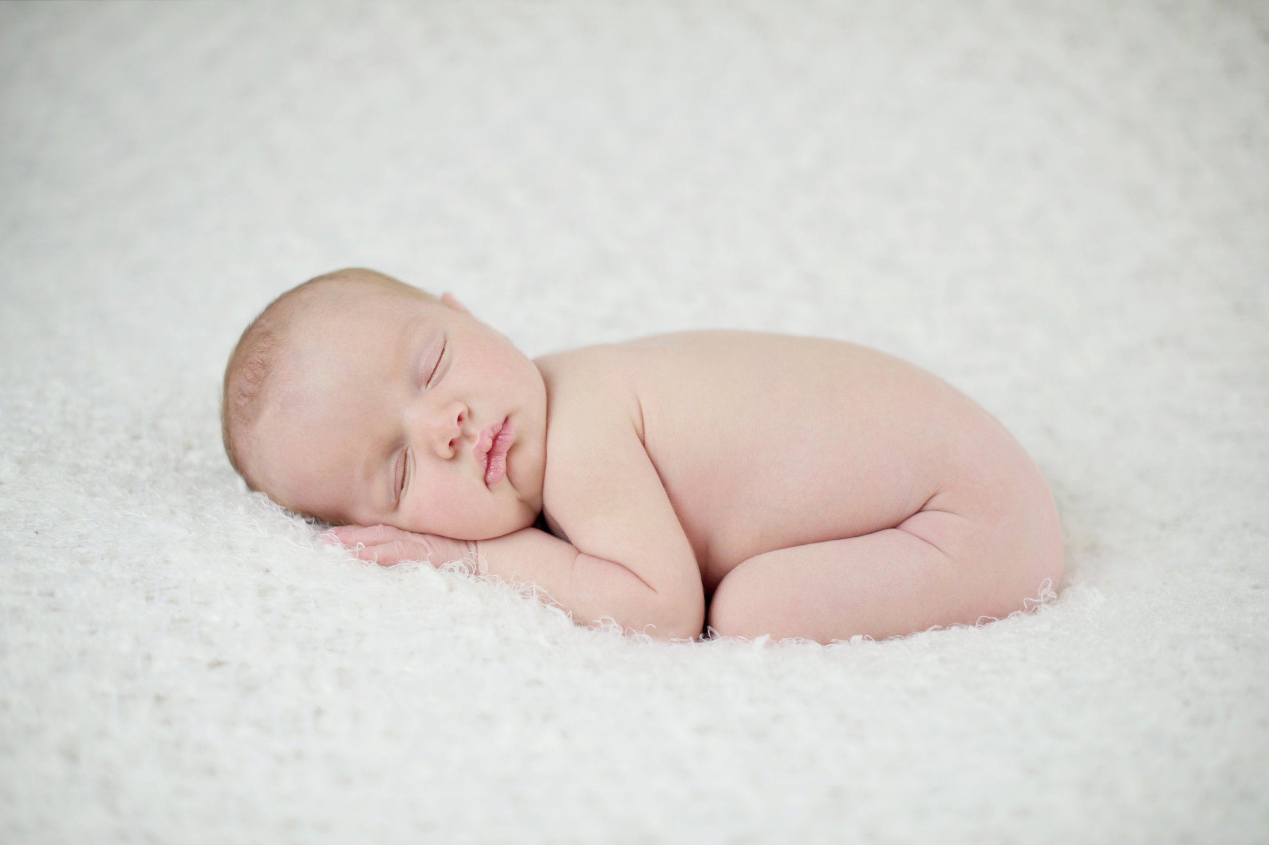 Portrait of a newborn baby sleeping on a soft white blanket.