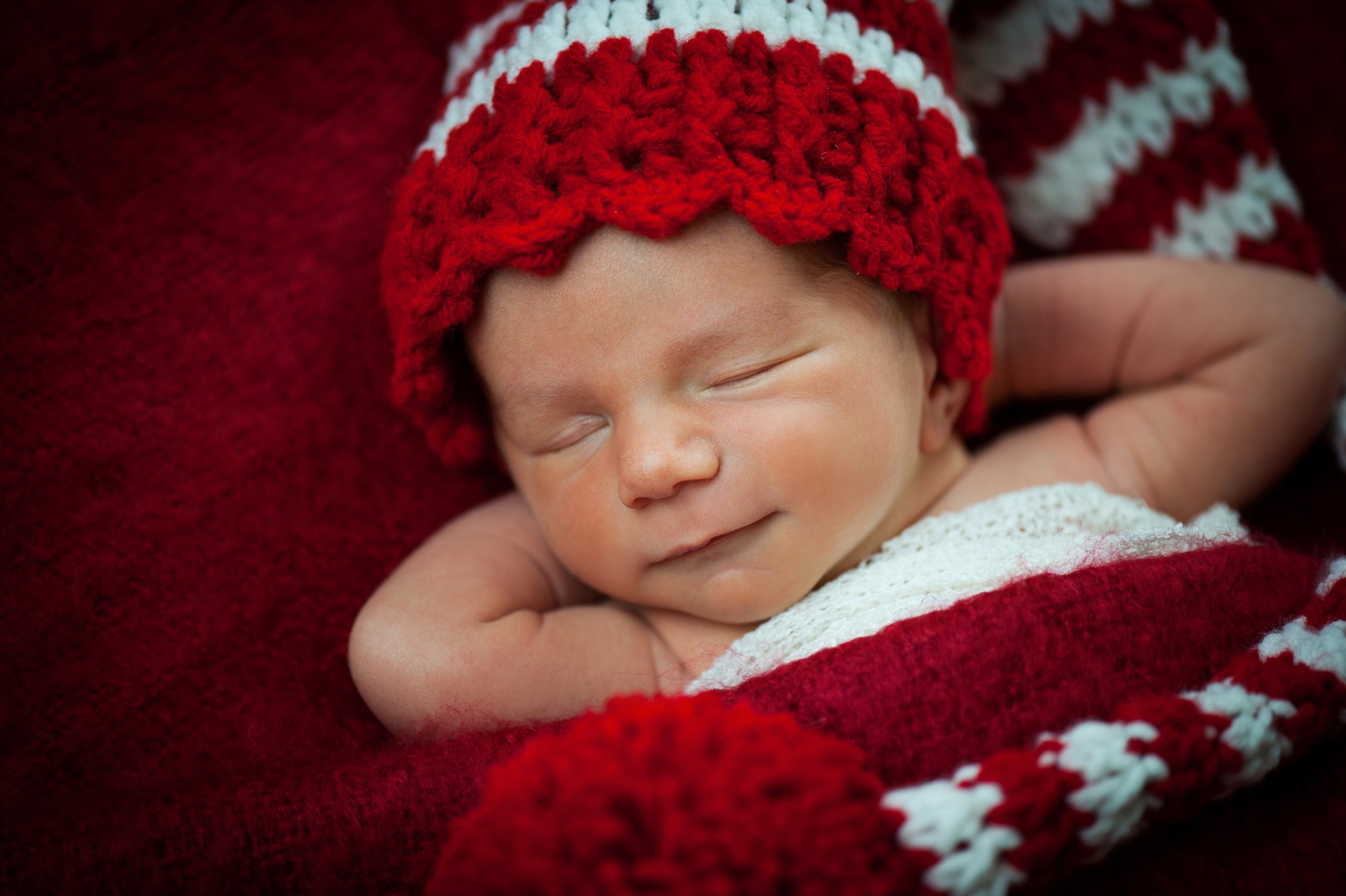 Newborn baby sleeping with a red and white crocheted hat, wrapped in a matching blanket.