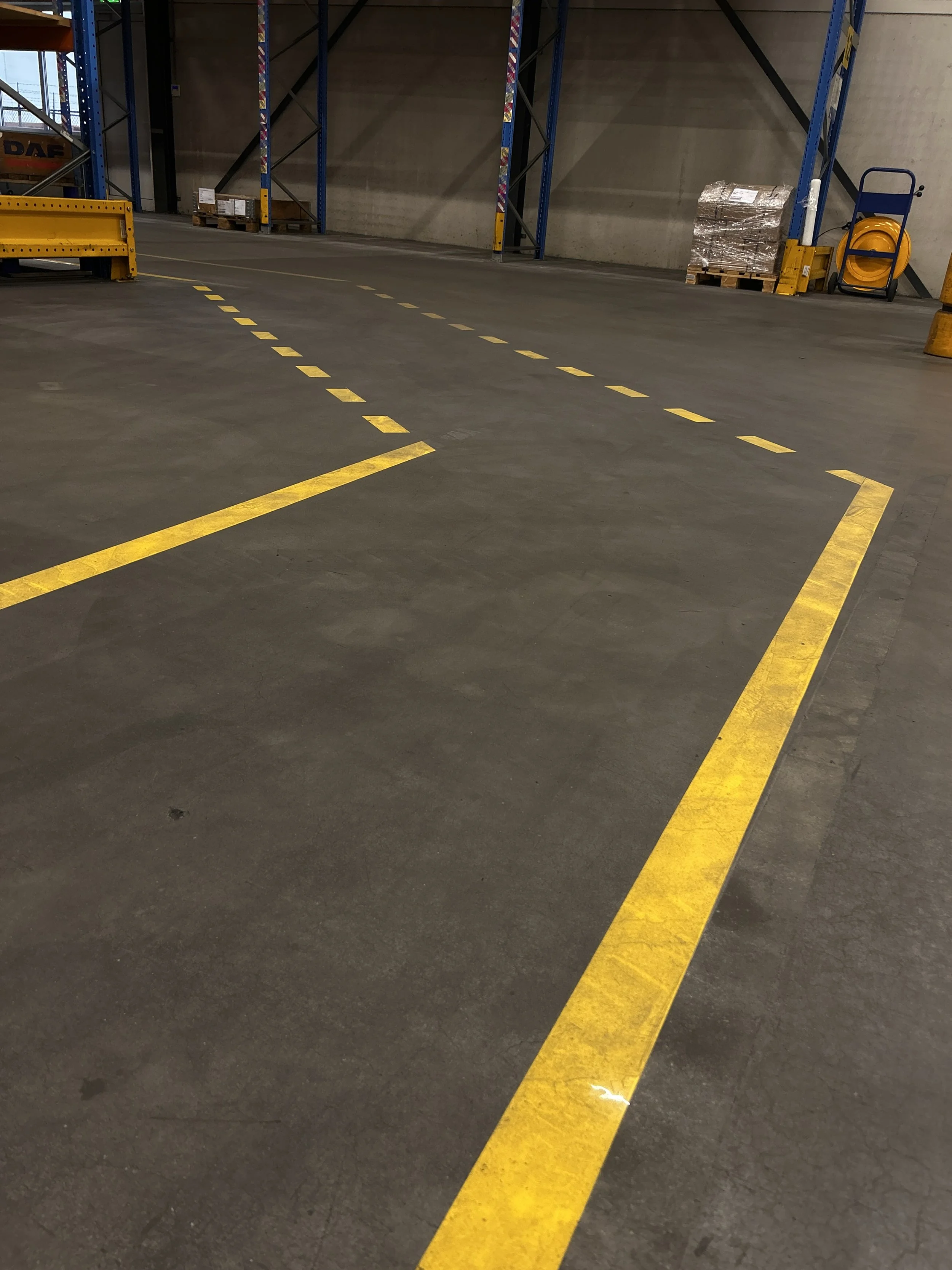 Empty warehouse with yellow parking lines and a pallet of wrapped goods in the background.