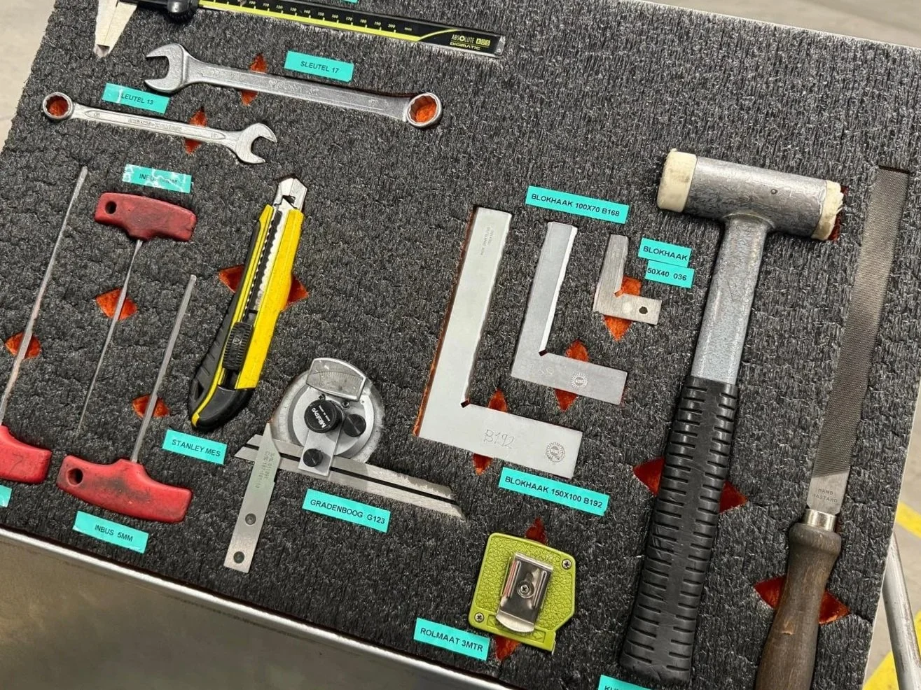 A foam-lined toolbox containing various tools, including wrenches, screwdrivers, a hammer, a tape measure, a square, and other measuring and hand tools, labeled with blue tags.