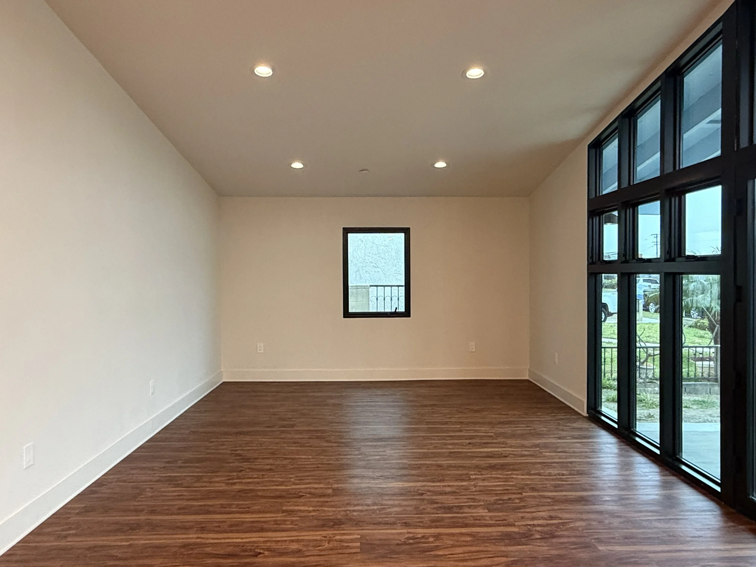 Empty room with hardwood floors, white walls, small window, and large glass doors on the right side leading outside.
