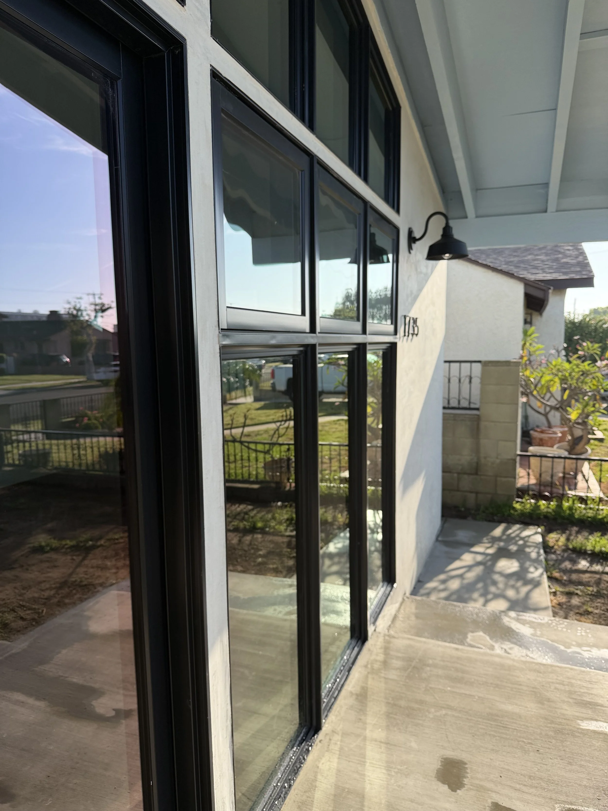 Exterior view of a house showing a sliding glass door, a small porch with concrete flooring, and a garden with potted plants and trees.