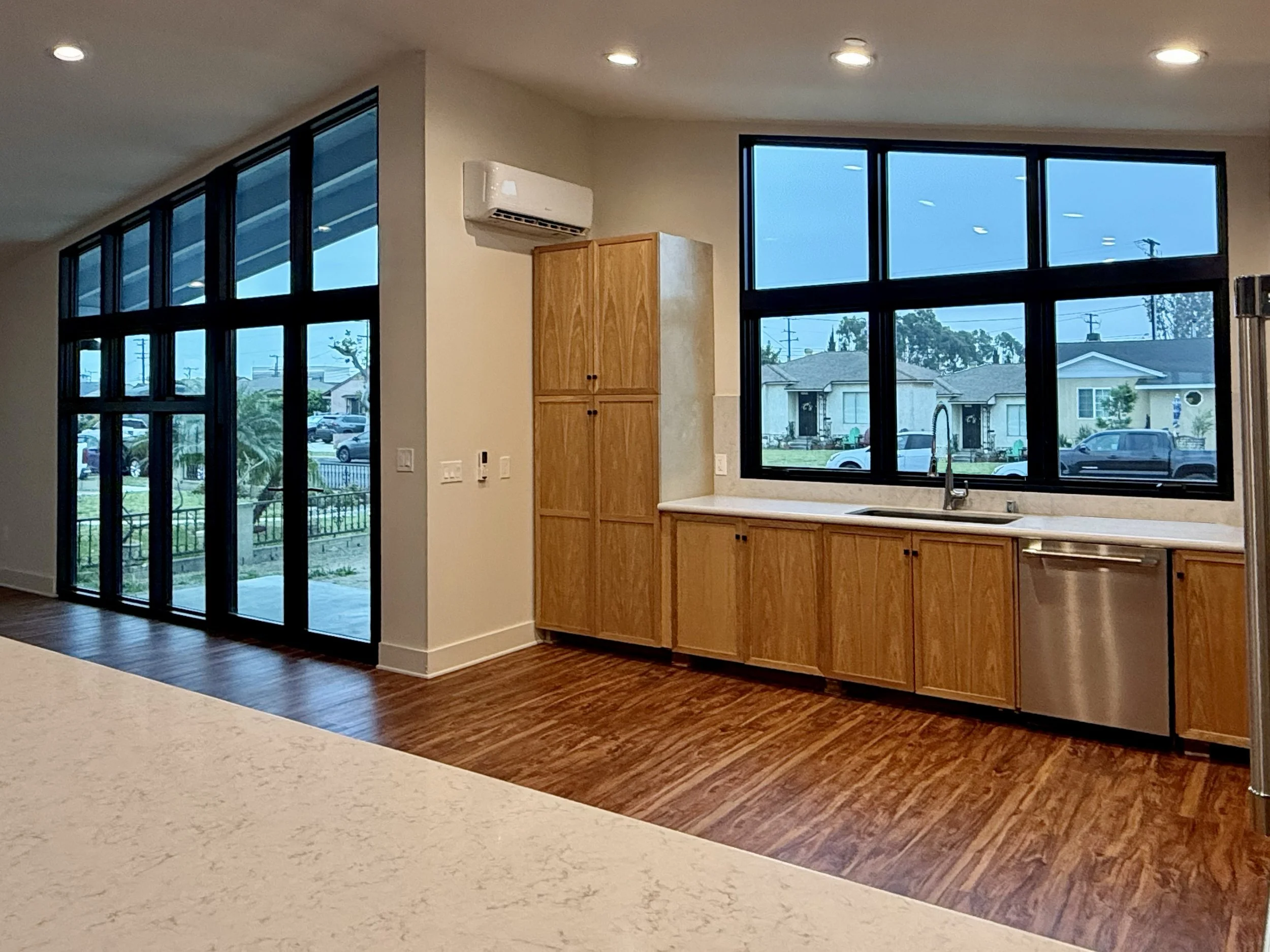 Kitchen with large black-framed windows, wooden cabinets, and white countertops.