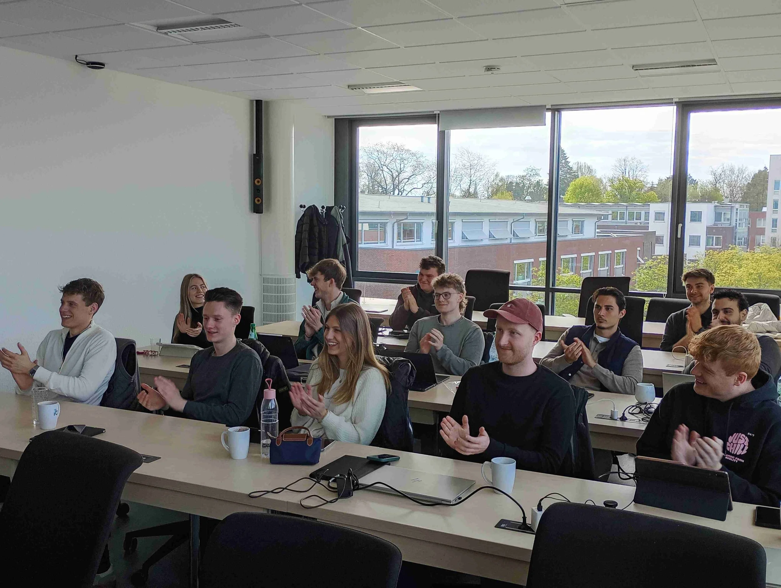 Eine Gruppe von Studierenden der Energiewirtschaft sitzt klatschend in einem Seminarraum der IBS Oldenburg. Sie blicken lächelnd in Richtung einer Präsentation.