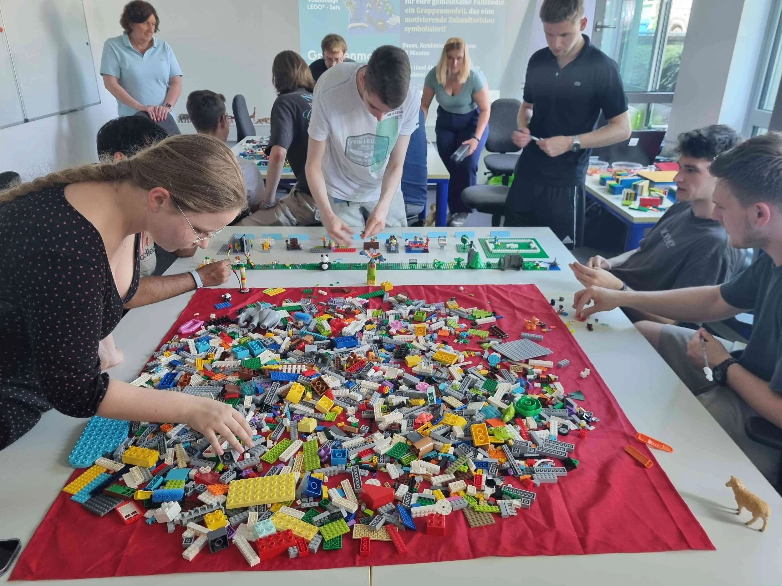 Eine Gruppe junger Menschen arbeitet an Tischen mit großen Haufen bunter Klemmbausteine an einem kreativen Workshop-Modell