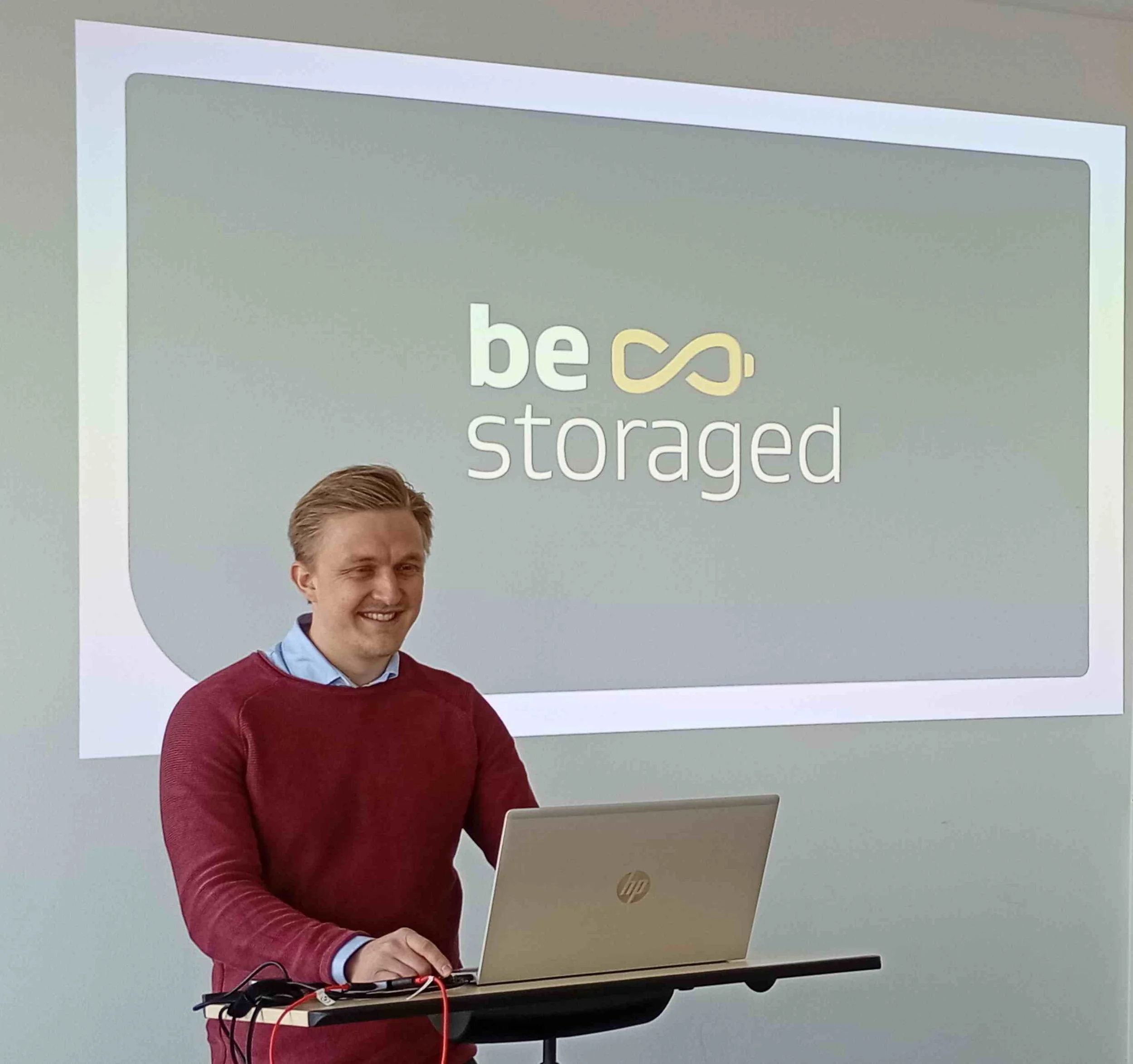 Ein lächelnder Gastdozent der Energiewirtschaft an der IBS Oldenburg hält eine Präsentation. Im Hintergrund ist das Logo „be storaged“ auf einer Leinwand zu sehen.