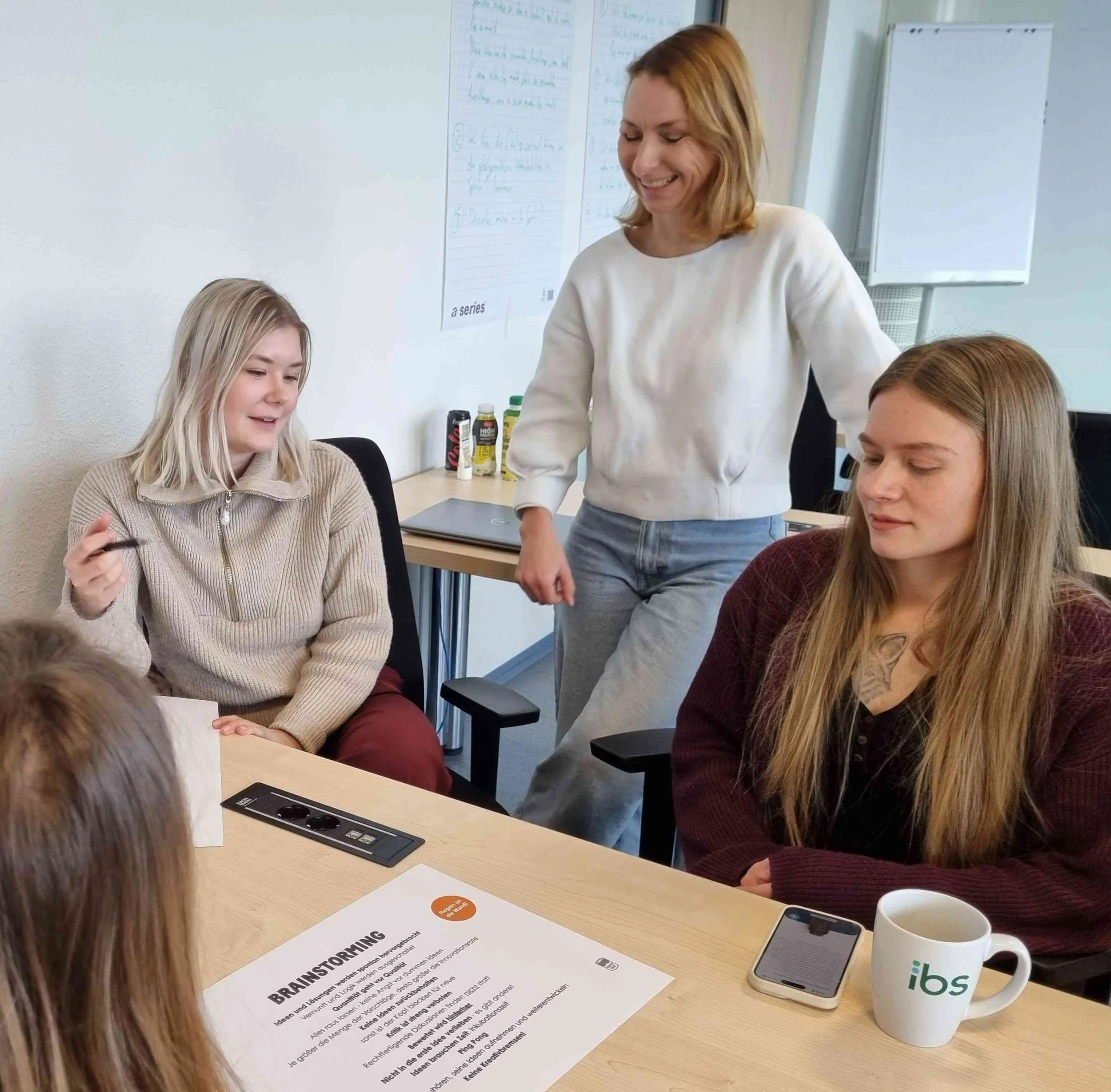 Eine Gruppe von drei Frauen der IBS Oldenburg bei einer Brainstorming-Sitzung an einem Tisch. Auf dem Tisch liegt ein Blatt mit der Aufschrift „BRAINSTORMING“. Eine Frau leitet an.